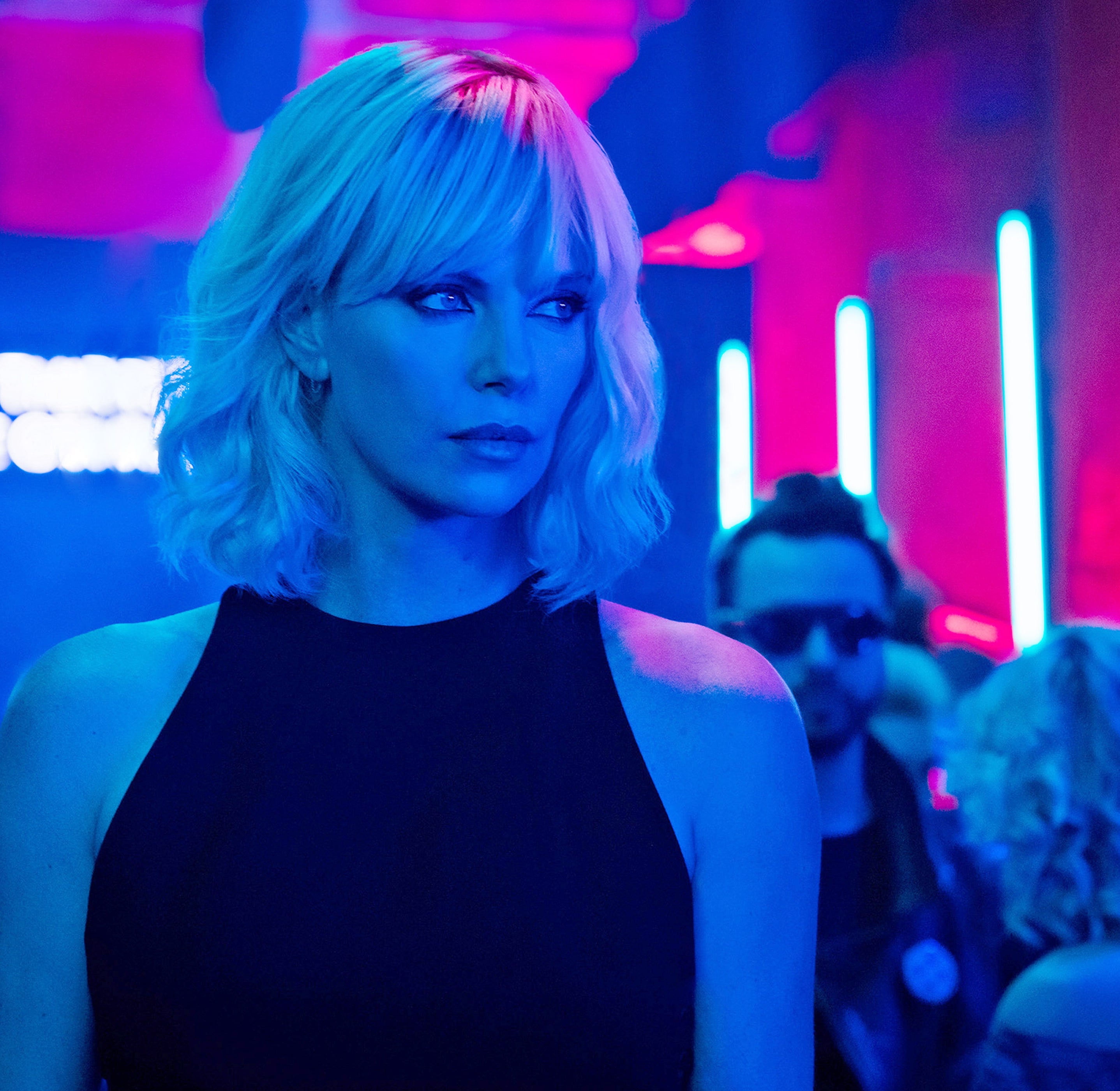 Person in a sleek black outfit at an event with neon lights and attendees in the background