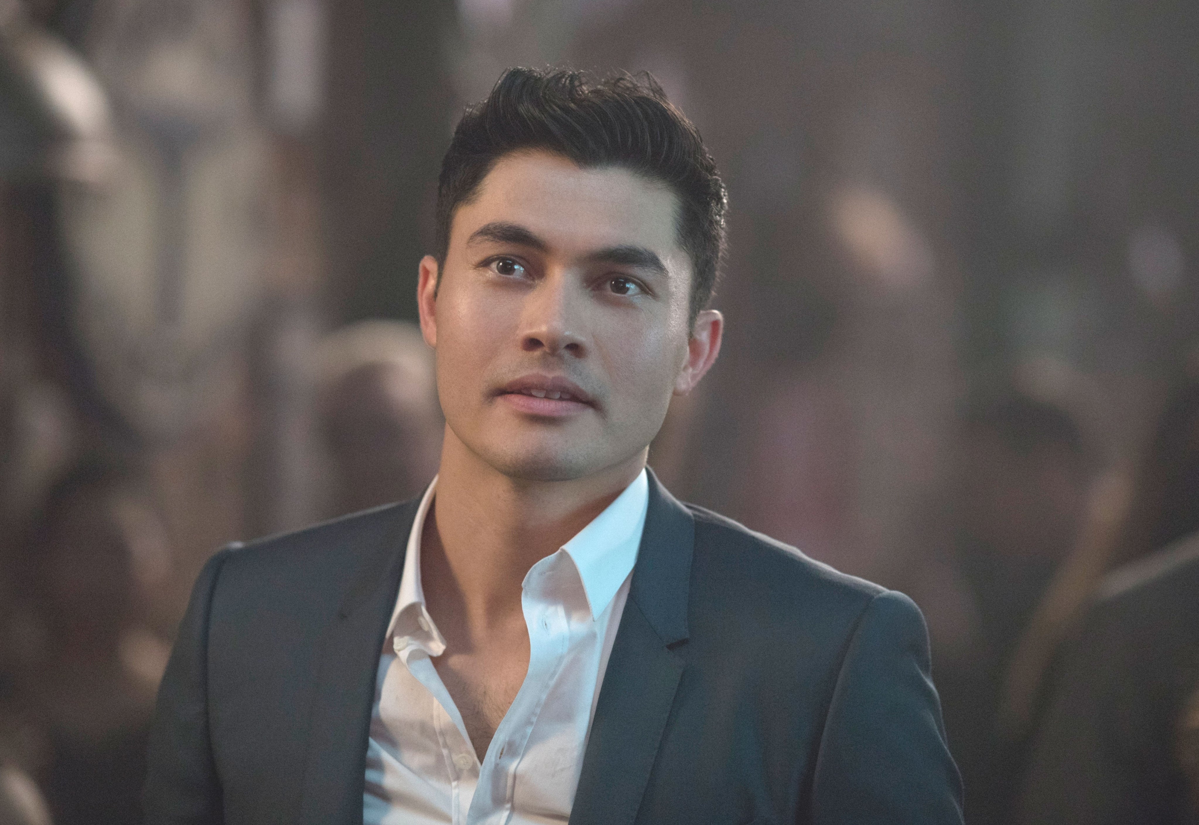 A person in a suit looks upwards with a thoughtful expression, in a dimly lit environment