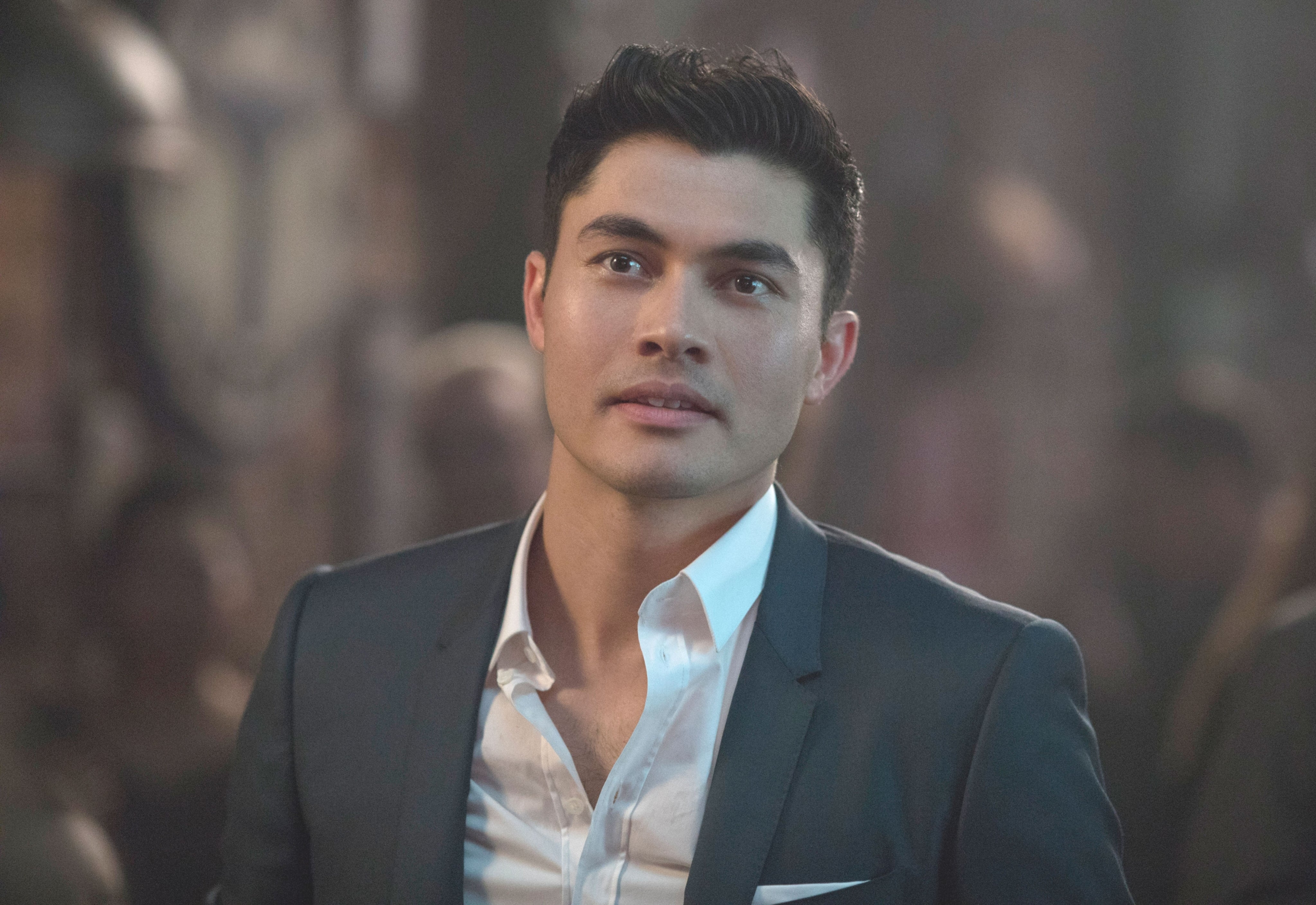 A person in a suit looks upwards with a thoughtful expression, in a dimly lit environment