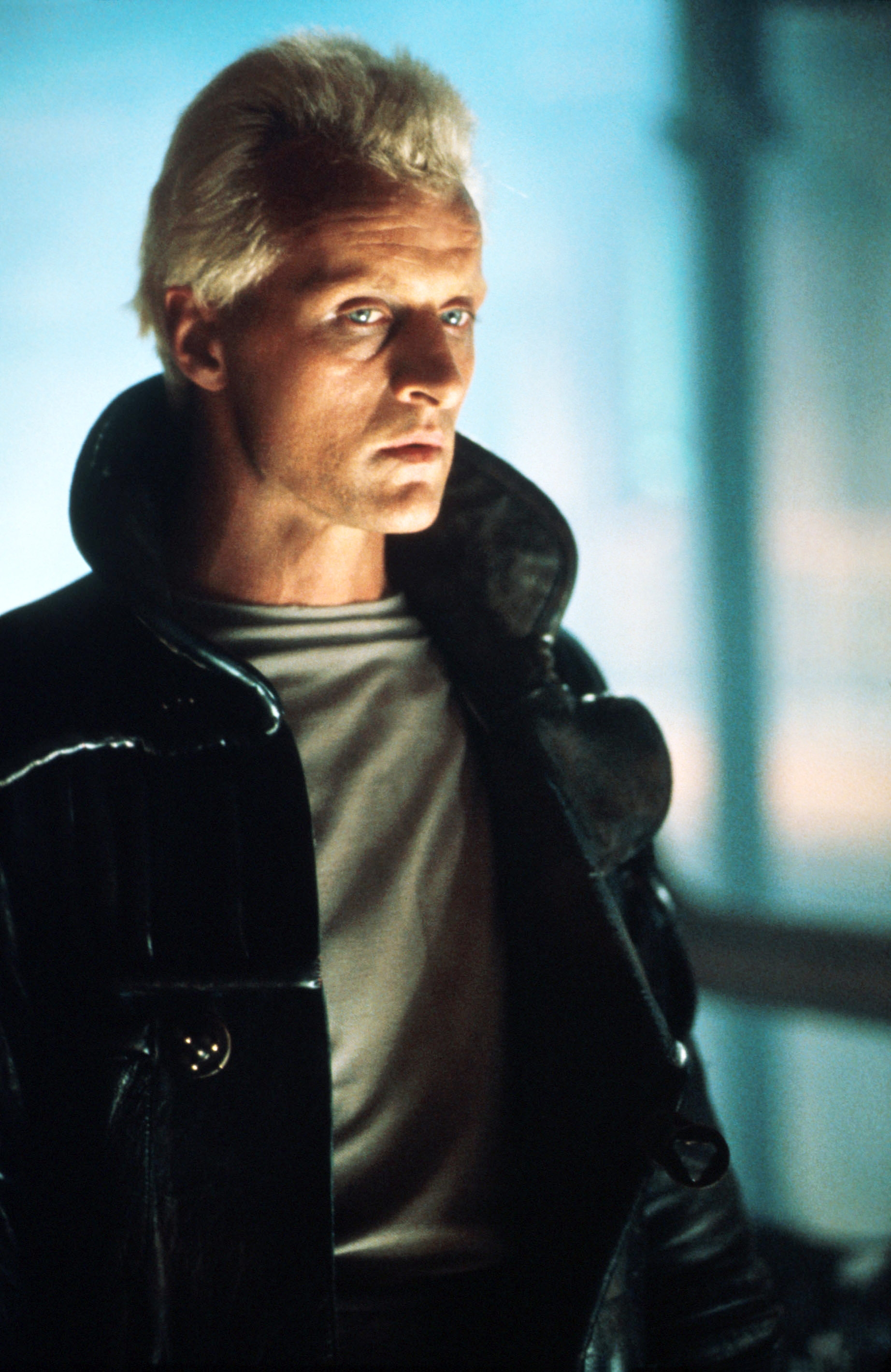 A person with short hair wearing a high-collared, futuristic jacket, looking intently forward, creating a dramatic atmosphere