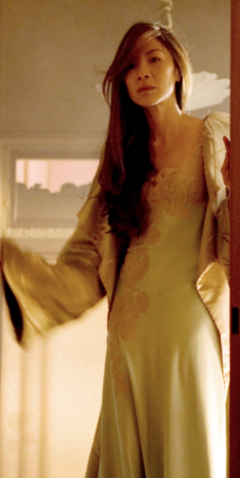 A person with long hair stands in a doorway, wearing an elegant robe and looking outward