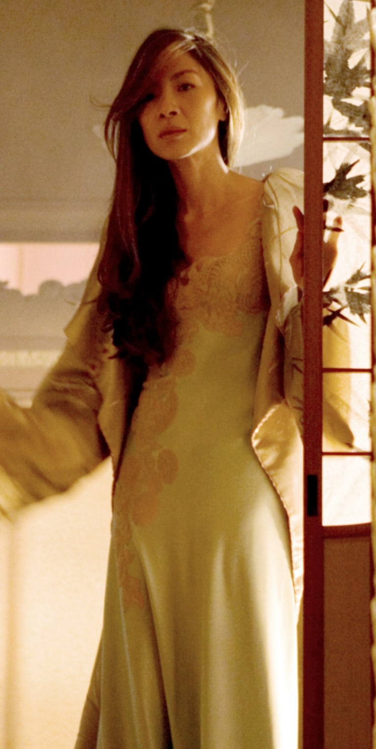 A person with long hair stands in a doorway, wearing an elegant robe and looking outward