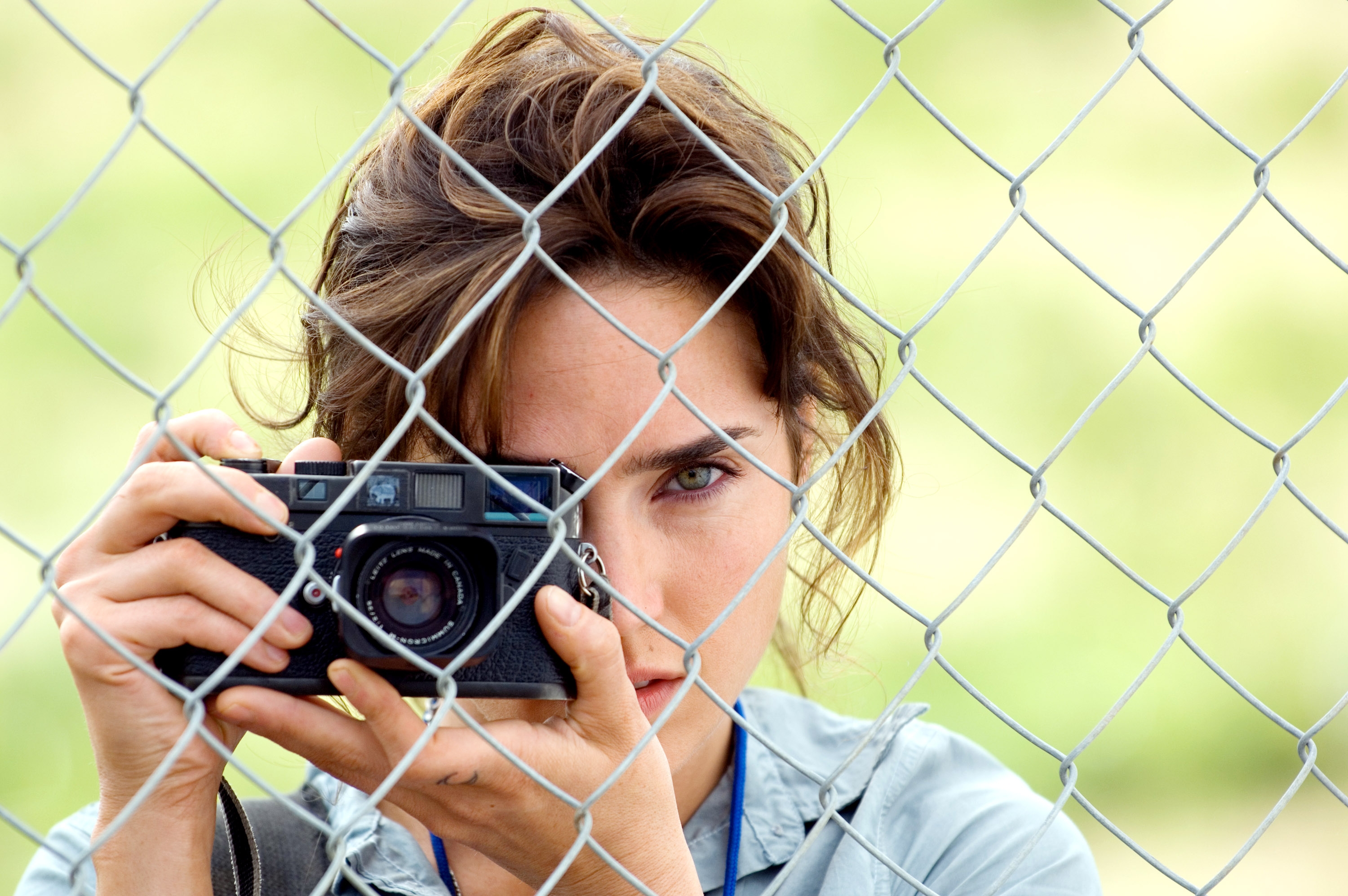 Person holding a camera peers through a chain-link fence, focusing on taking a photo