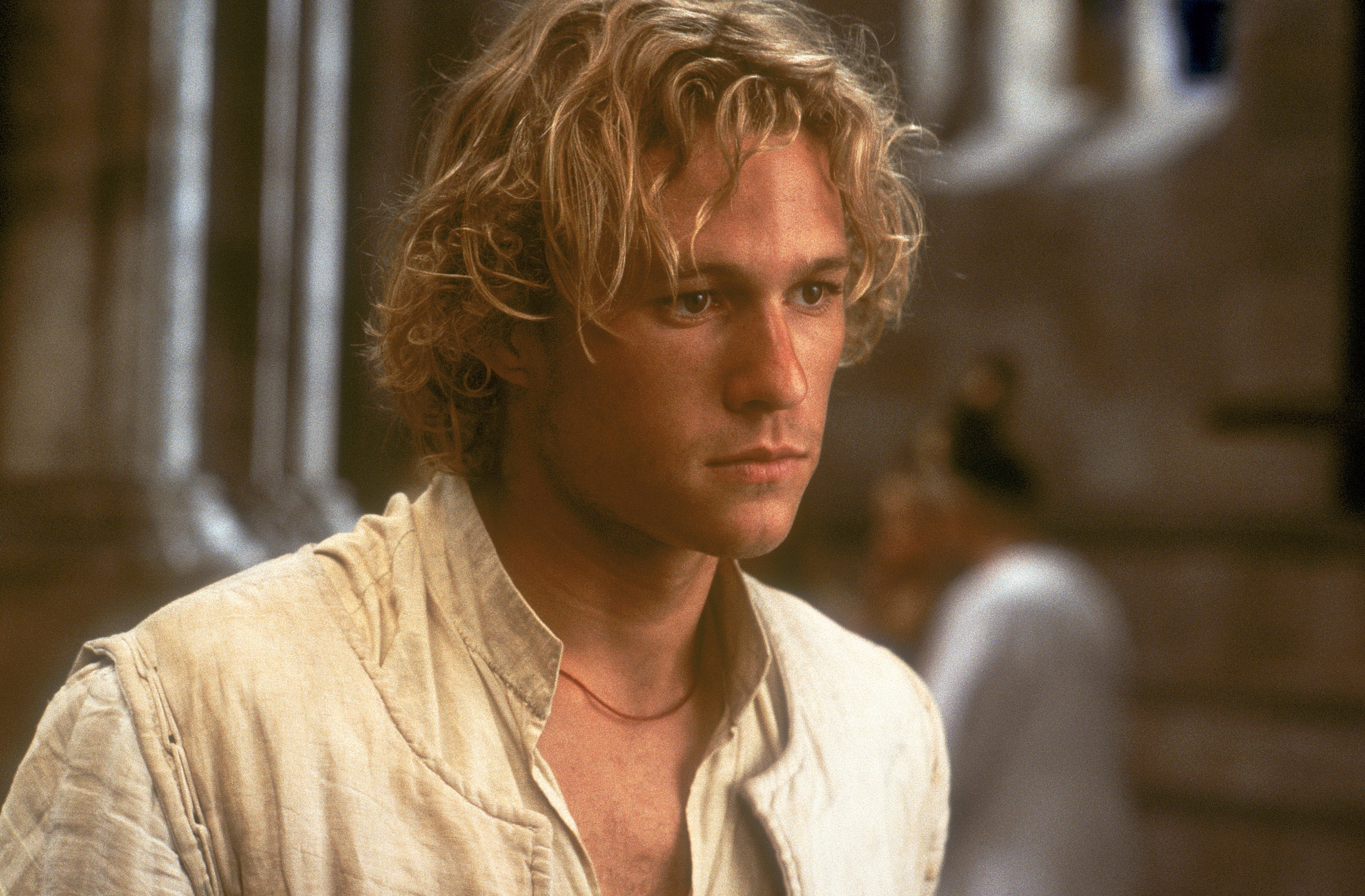 A person with tousled hair wearing a period costume shirt, looking contemplative, possibly on a film set