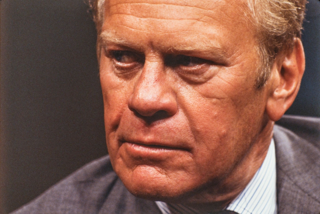 An older man in a suit with a serious expression, looking to the side