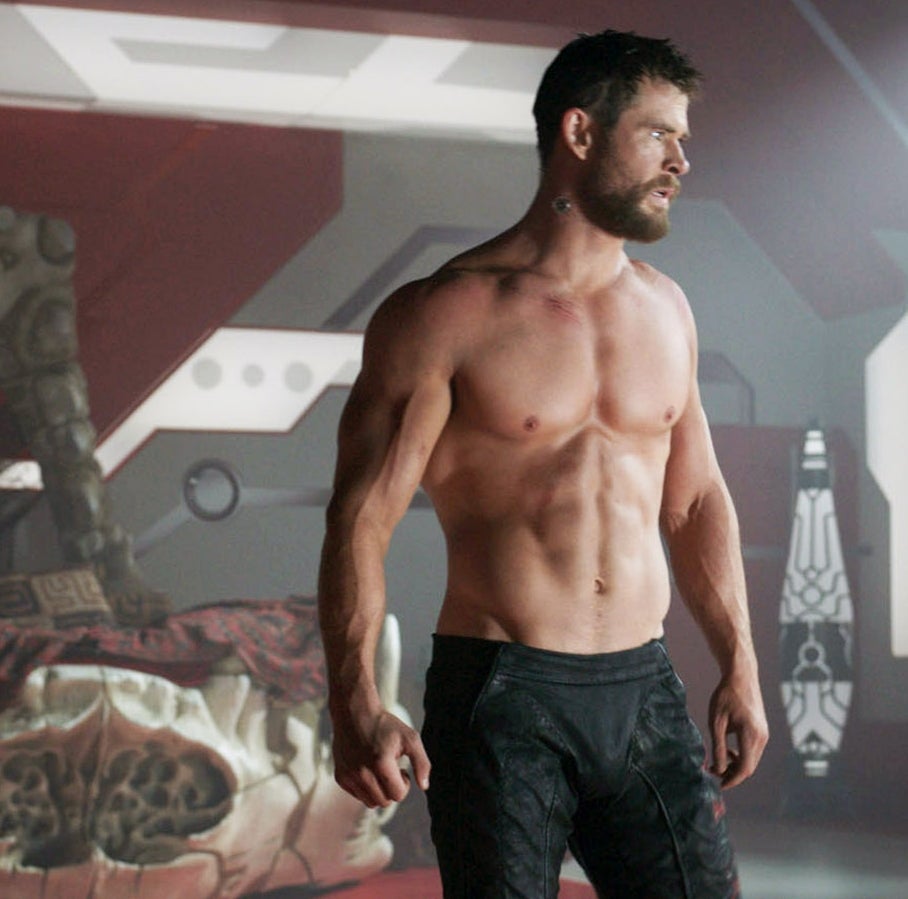A shirtless man with short hair and muscular build stands in a futuristic setting, looking serious