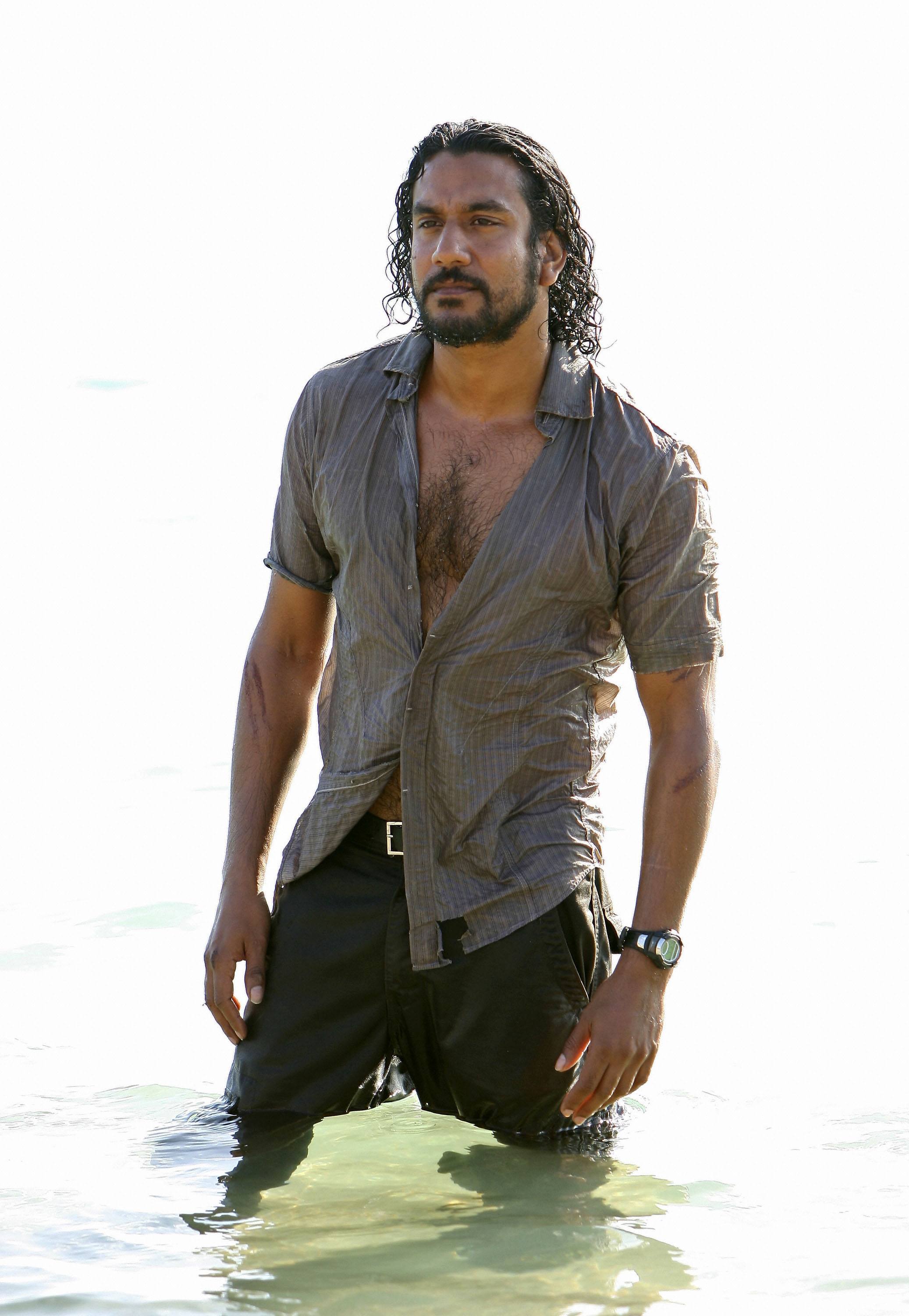 Person standing in water, wearing a partially open shirt and dark pants, with wet hair