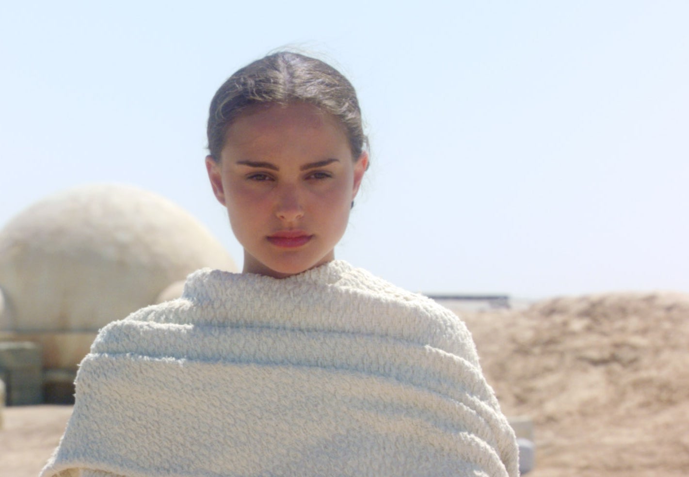 Person wearing a textured wrap stands in a desert setting with round, dome-like structures in the background