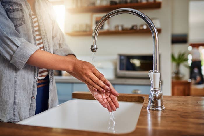 Person washing hands under a kitchen sink tap in a home setting, demonstrating hygiene practices related to food preparation