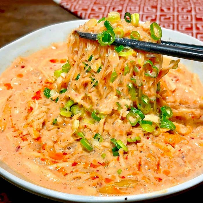 クリーミーなソースに絡めたラーメンを箸で持ち上げるシーン。上には刻みネギがトッピングされています。