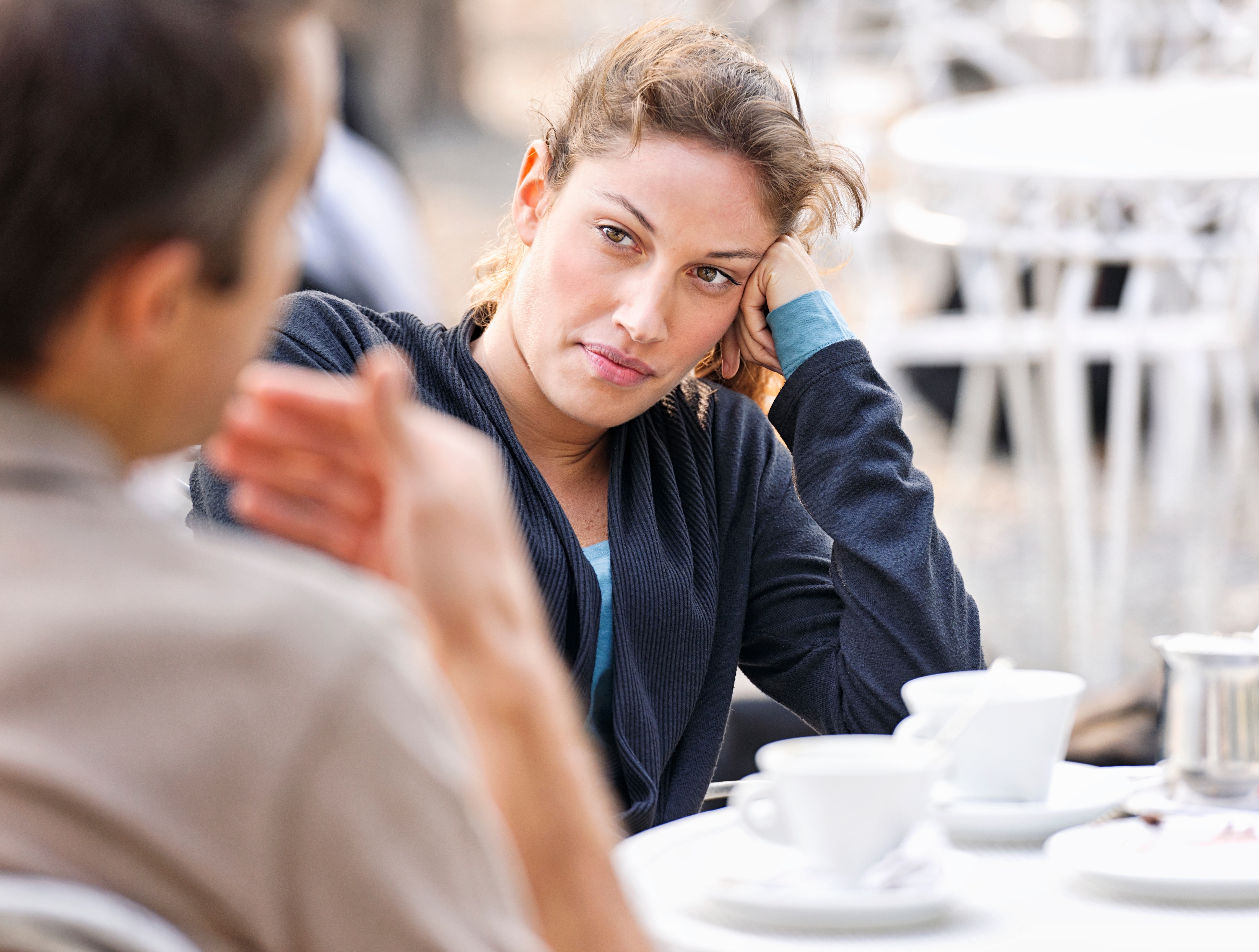Woman attentively listens to man at outdoor cafe, resting her head on her hand