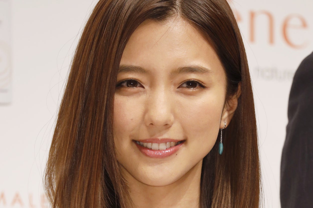 女性が微笑んでカメラを見つめている。彼女はシンプルな白いトップを着ている。