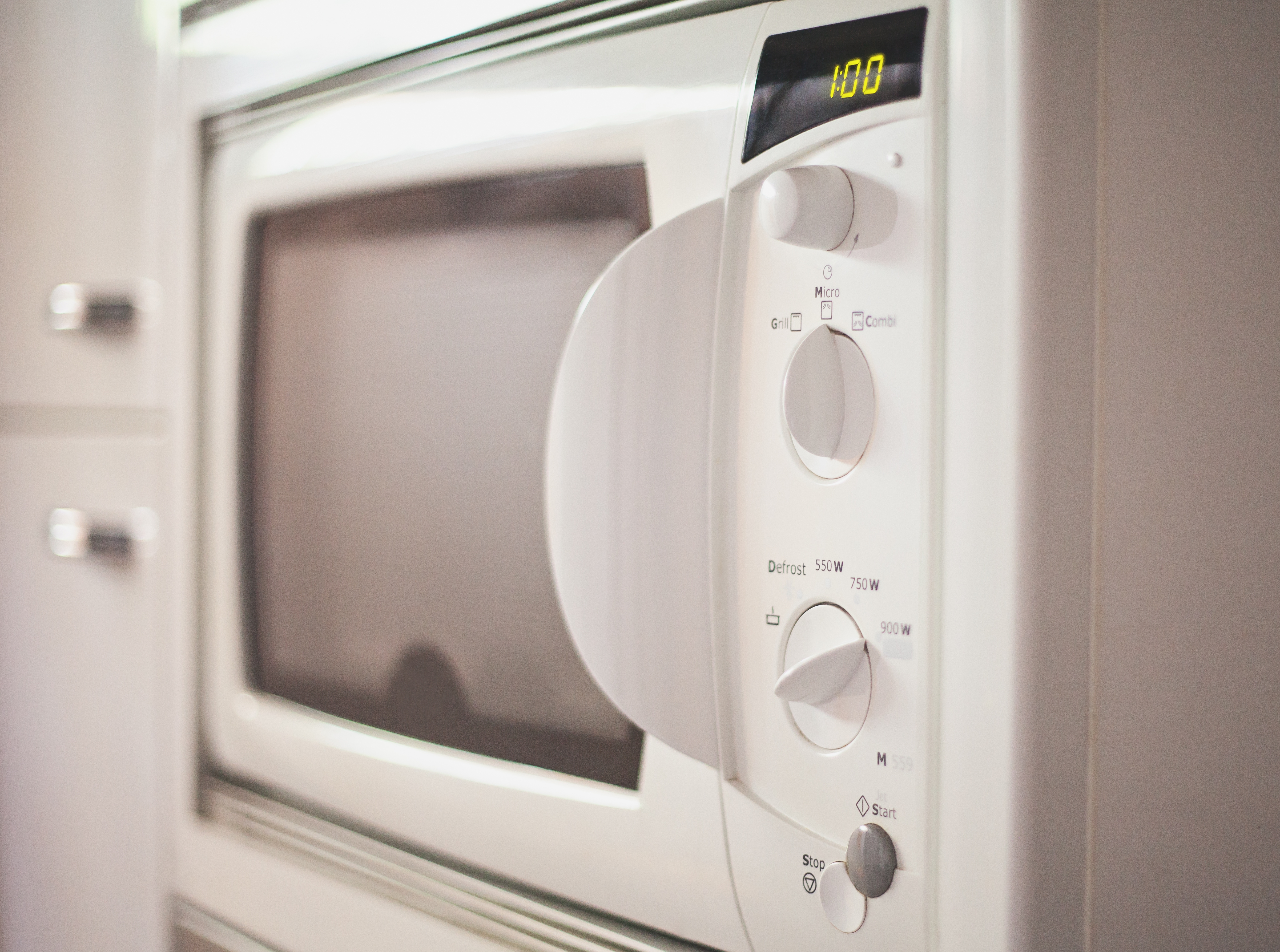 Close-up of a microwave with a digital display showing 1:00. The control panel has various settings and a large handle
