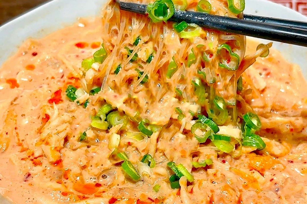 クリーミーなラーメンを箸で持ち上げている。ネギがトッピングされ、鮮やかな食感が強調されている。