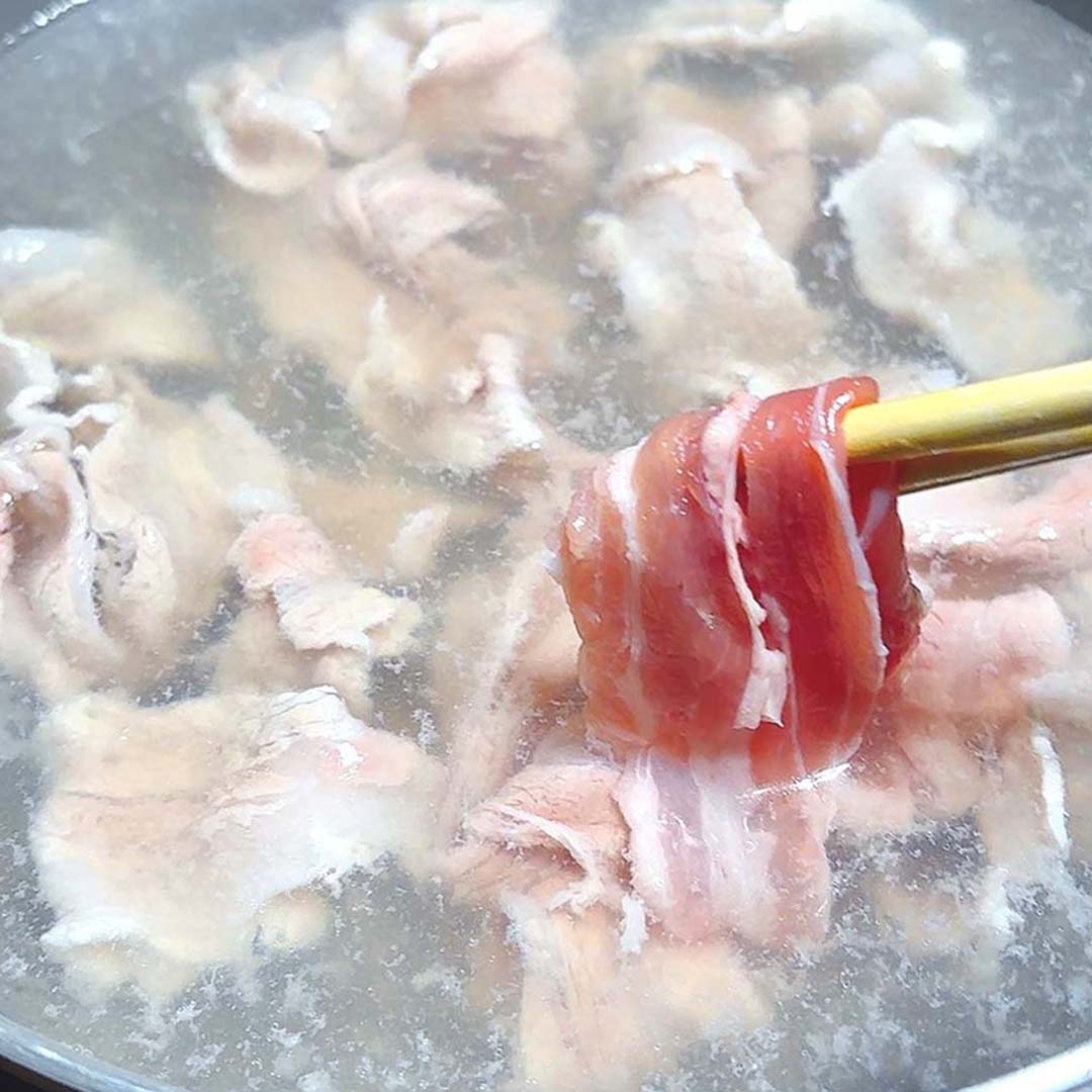 日本の鍋料理で、薄切り肉を煮込んでいる様子。箸で肉を持ち上げている。