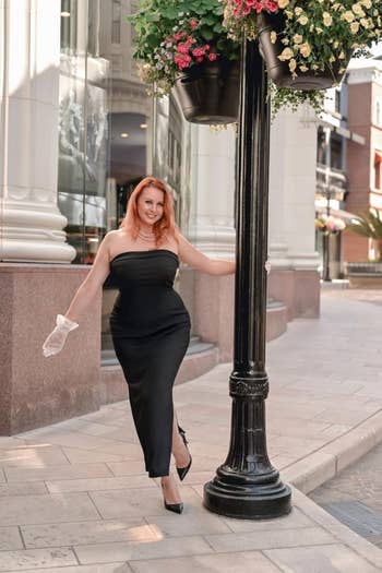 Person successful a strapless achromatic evening gown and gloves stands outdoors by a lamppost, showcasing an elegant buying outfit