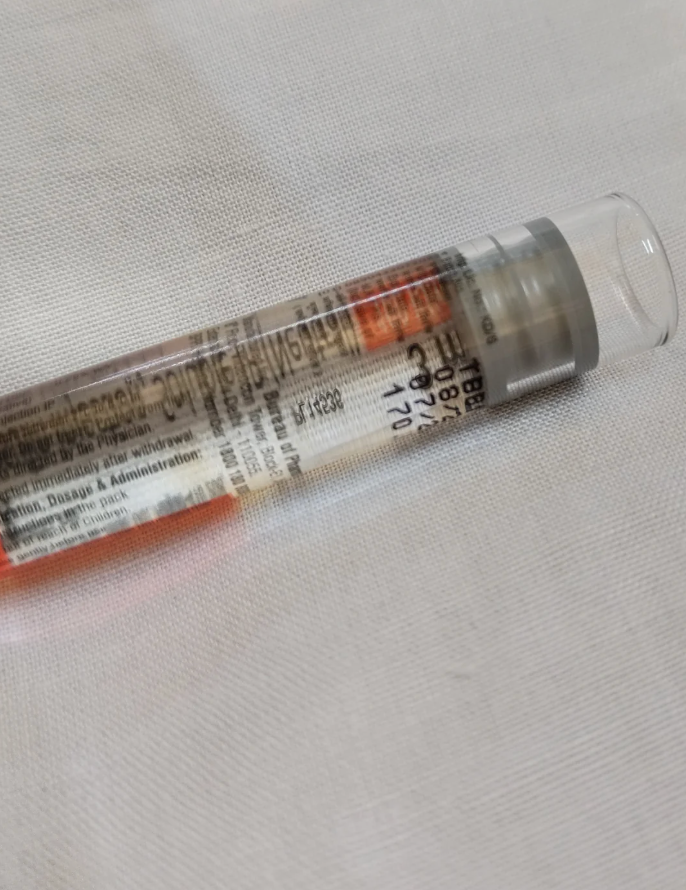 A clear vial with a white label and small black text, partially visible, positioned on a white surface