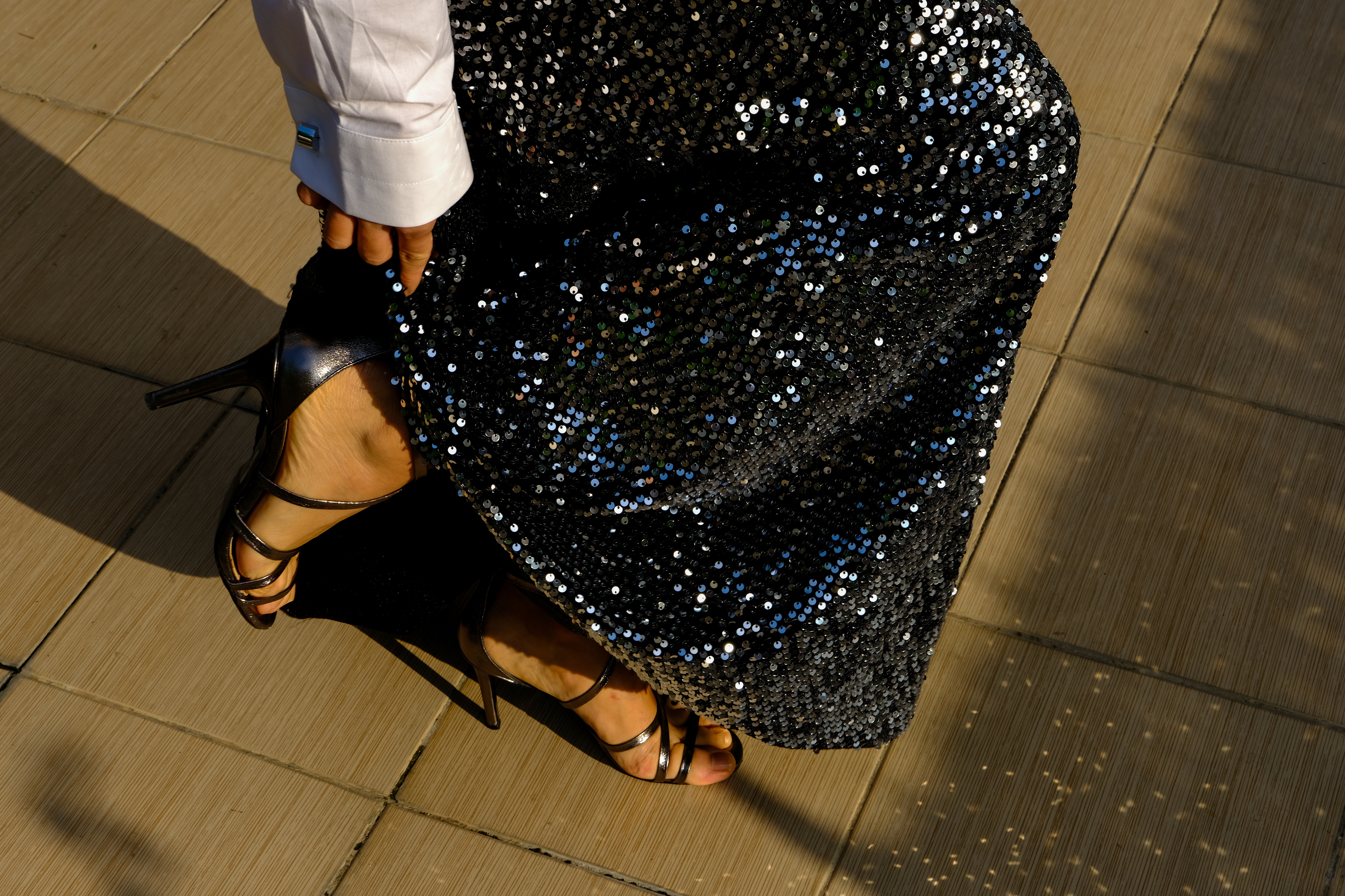 Person in a sequin dress and strappy high heels, adjusting the hem while walking on a tiled surface