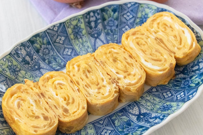 皿に盛られた玉ねぎ入り卵焼き。背景に玉ねぎが2個。