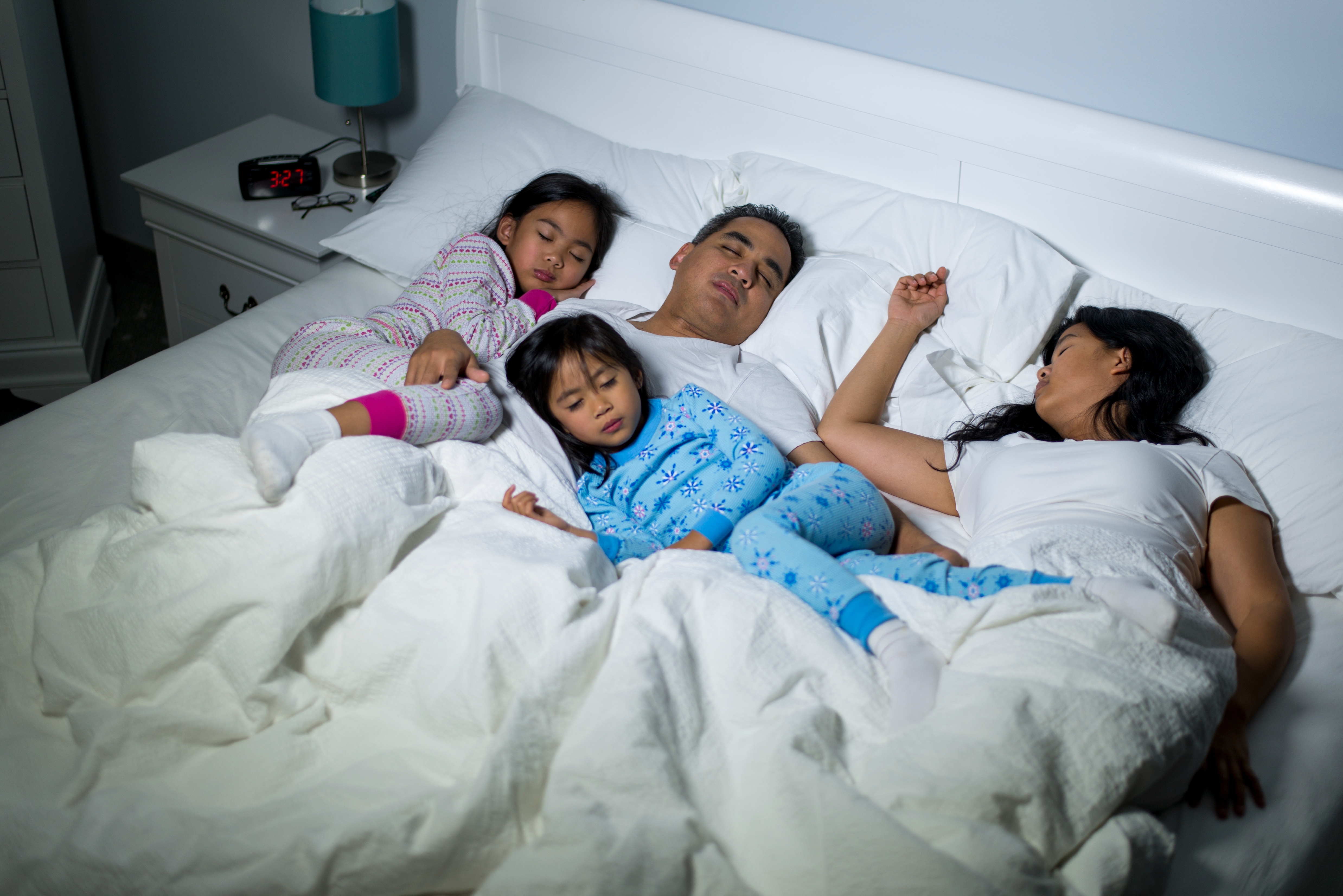 Family of four sleeping peacefully in bed, dressed in pajamas