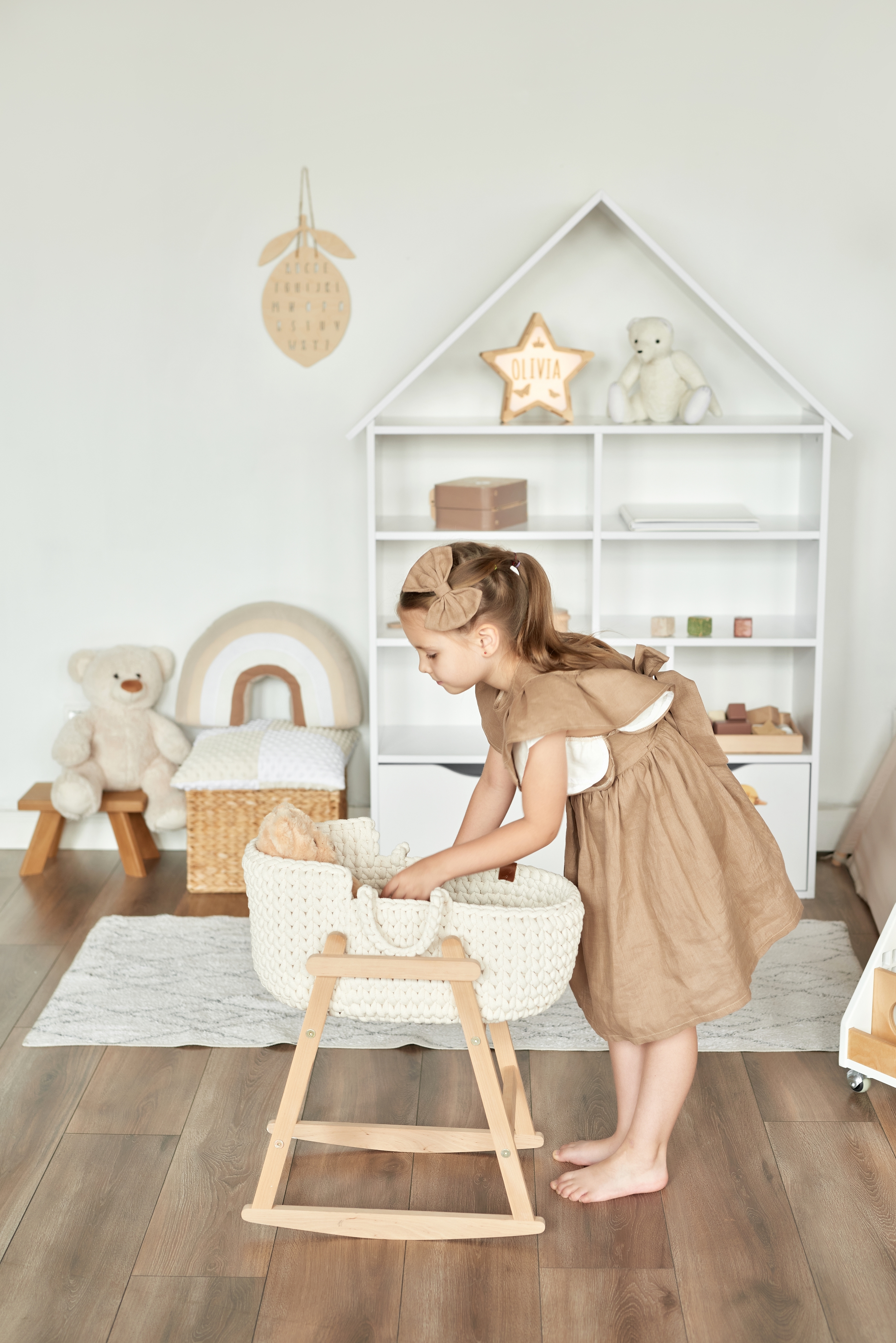 Child in a cozy nursery tending to a doll in a cradle, with shelves, toys, and decor around