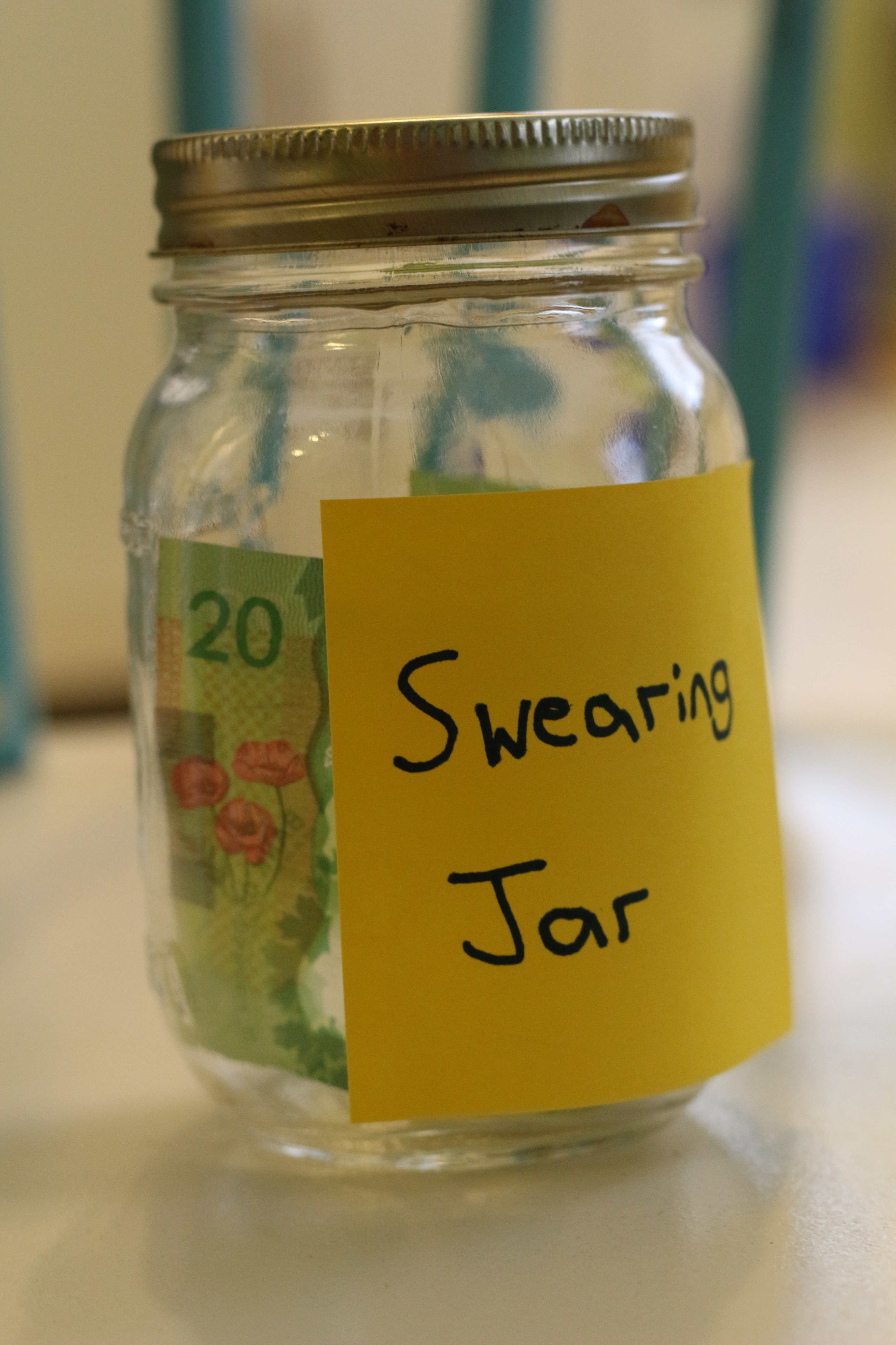Glass jar labeled &quot;Swearing Jar&quot; containing a visible 20-note inside