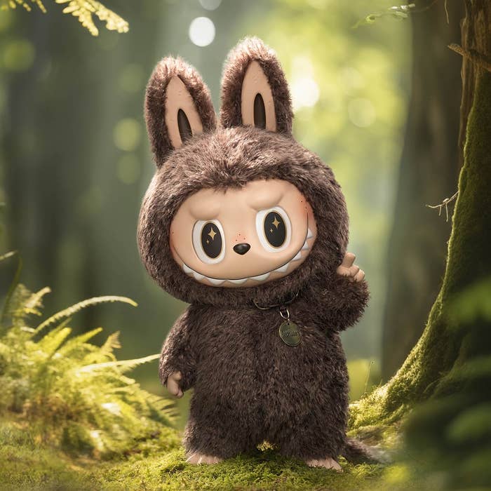 Cute cartoon character in a fuzzy animal costume stands in a lush forest, smiling mischievously with one hand raised in a friendly gesture
