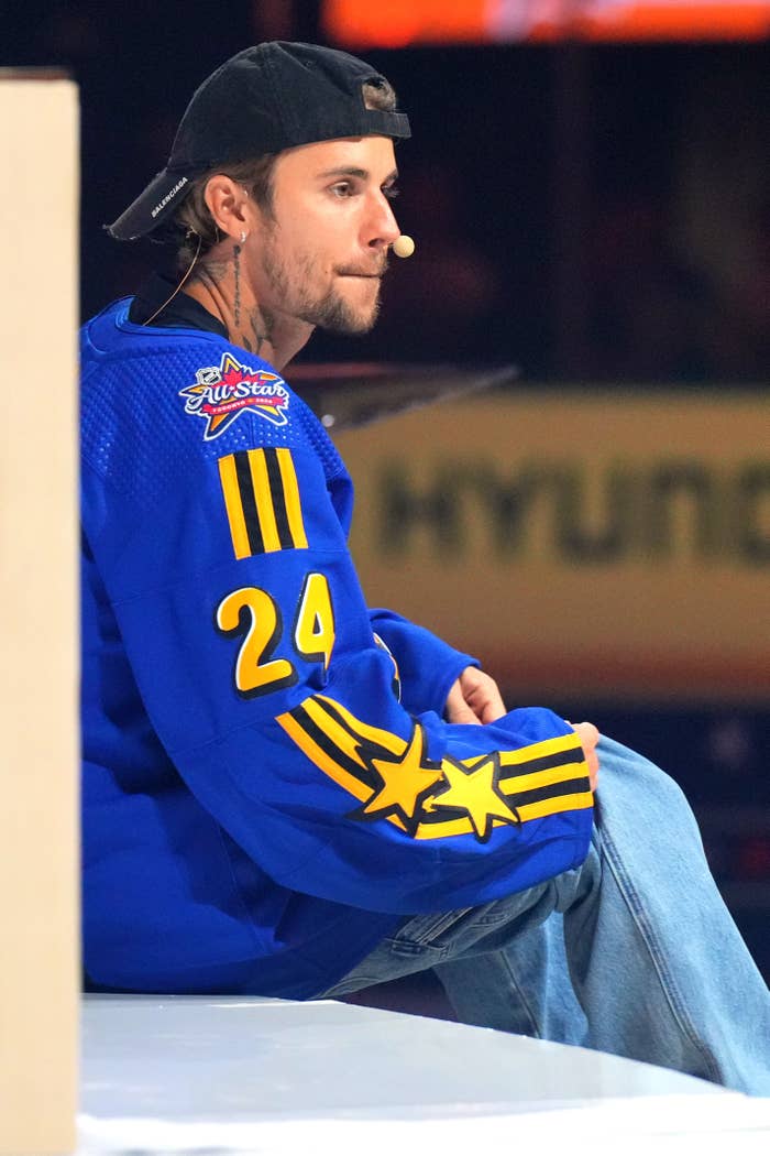 Justin Bieber in a hockey jersey, sitting with headset on at an event