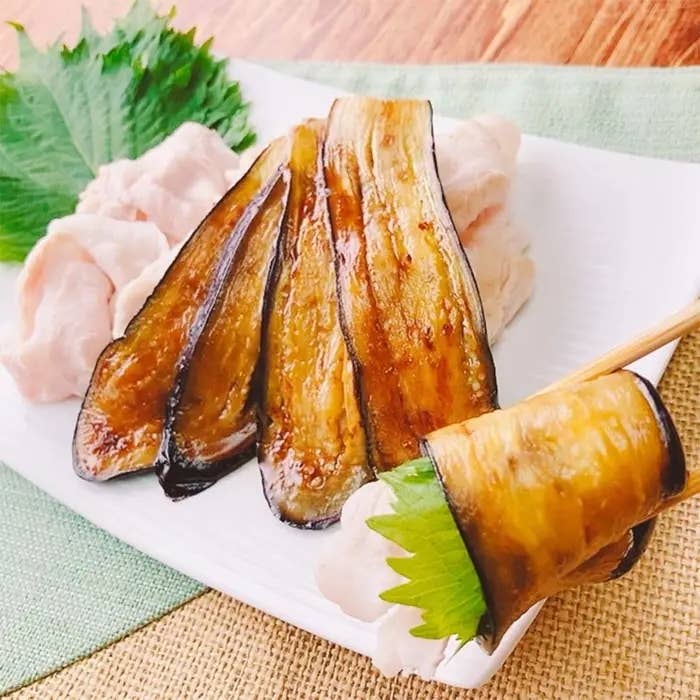 焼きナスとシソで豚肉を包んだ料理が白い皿に盛られた画像。食材が彩り豊かに飾られている。