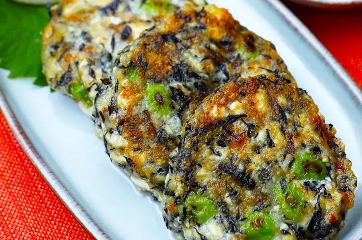 白い皿に盛られたヒジキと野菜の焼き物。添えられたレモンのくさびとソースが後ろに見える。