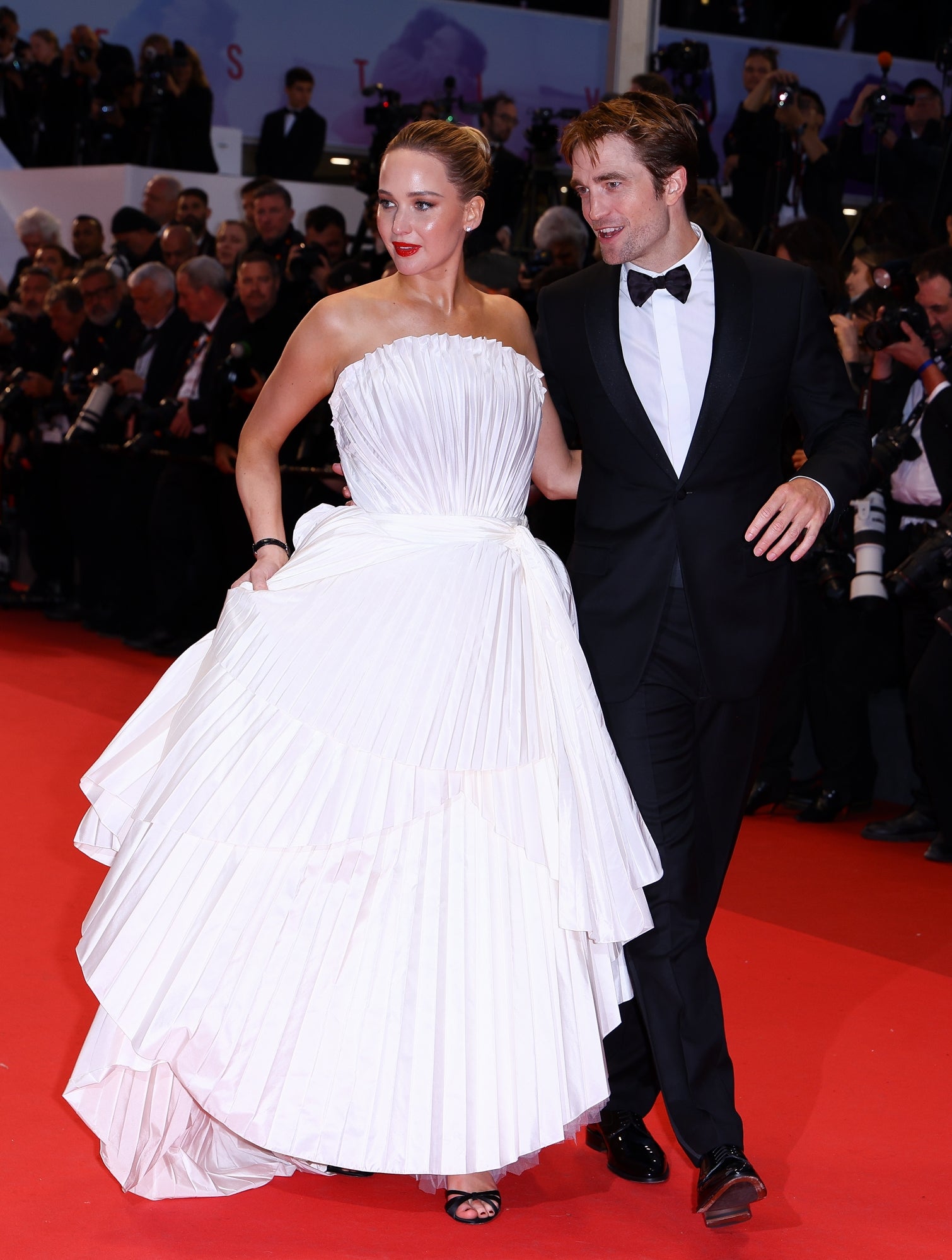 Jennifer Lawrence in a dress with a fan design while walking down the red carpet with Robert Pattinson