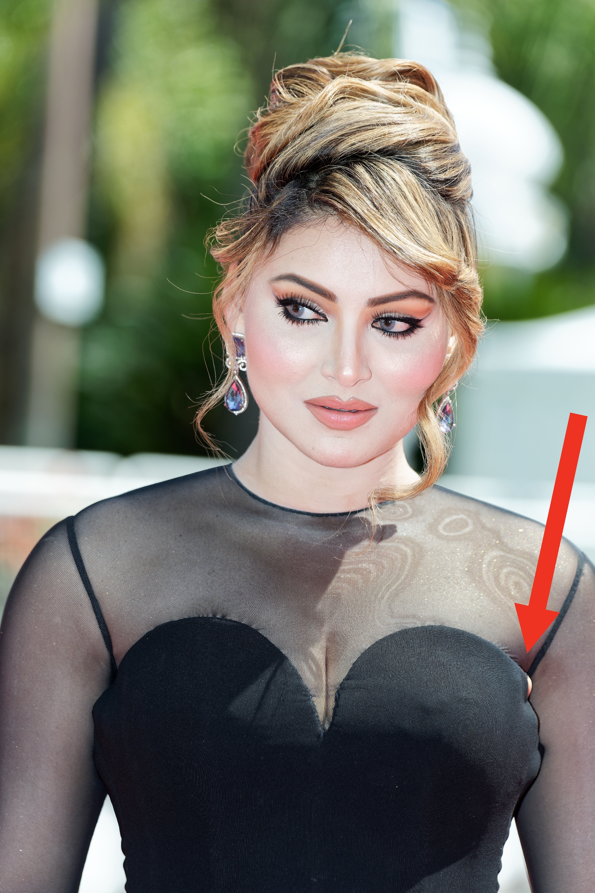 Urvashi Rautela on the red carpet wearing a sheer dress with heart-shaped bodice, styled hair, and statement earrings