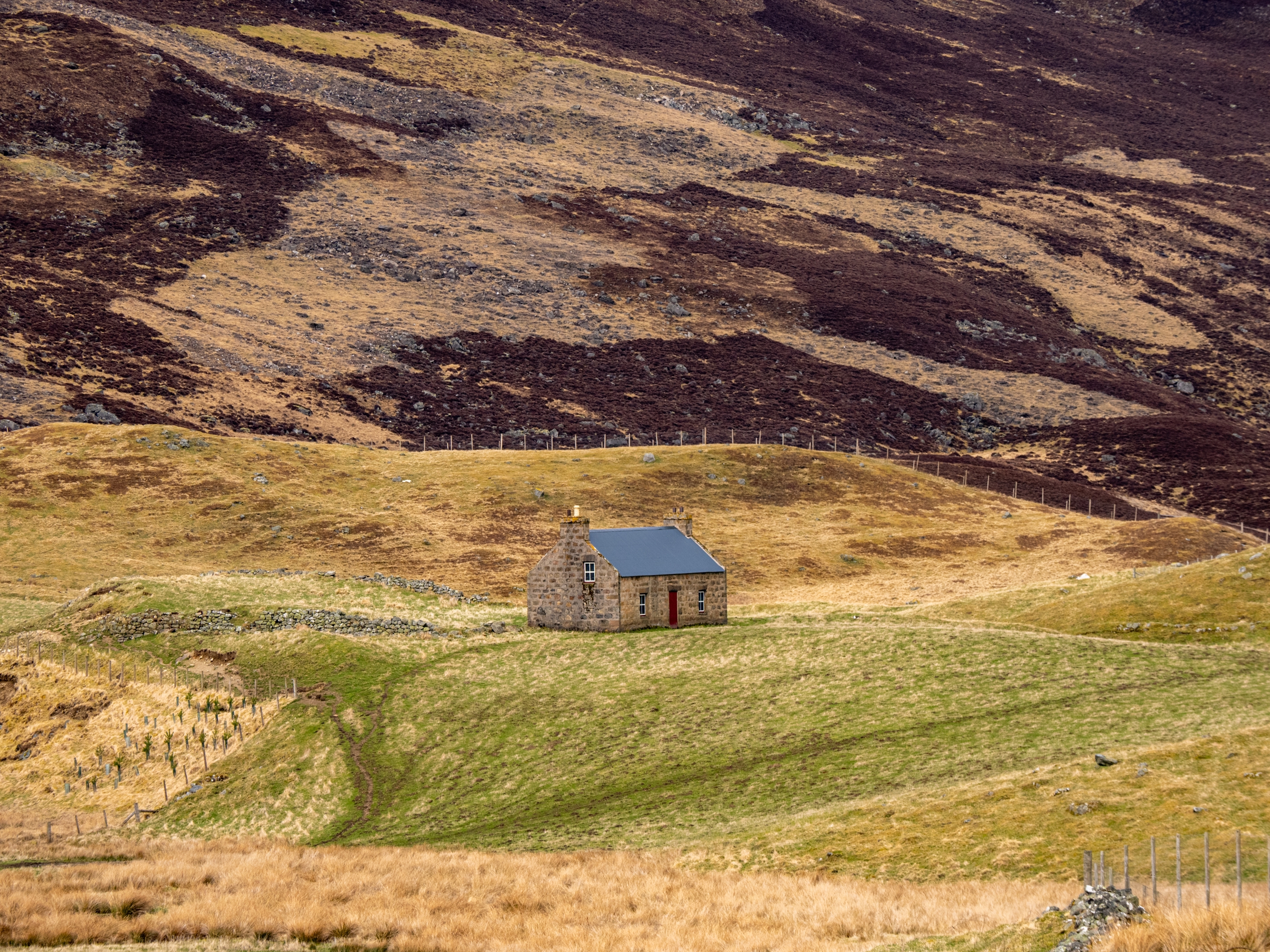 Small stone cottage stands alone in a vast, hilly landscape with a moorland backdrop