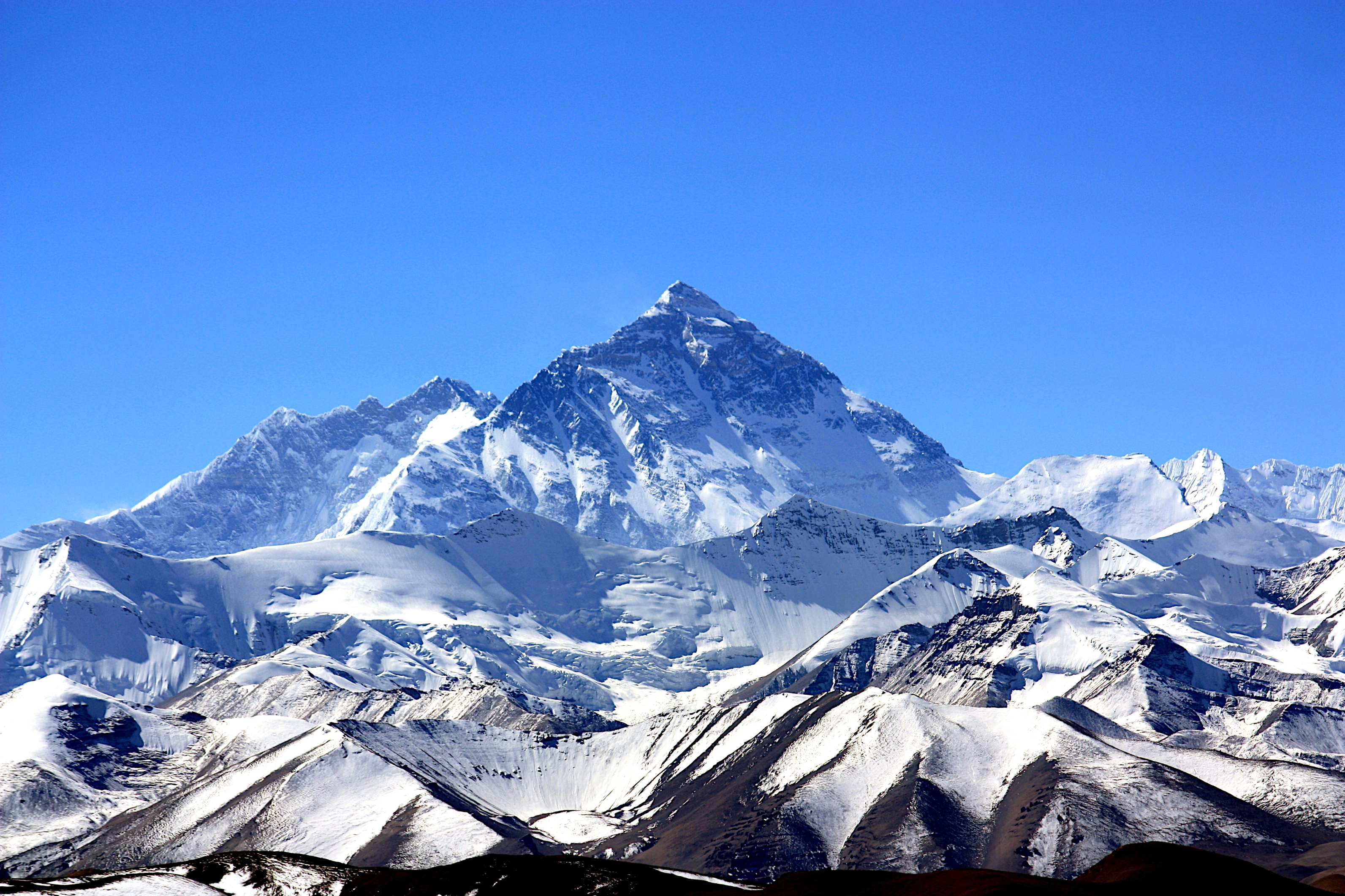 Snow-covered mountain range with a prominent peak towering in the background under a clear sky