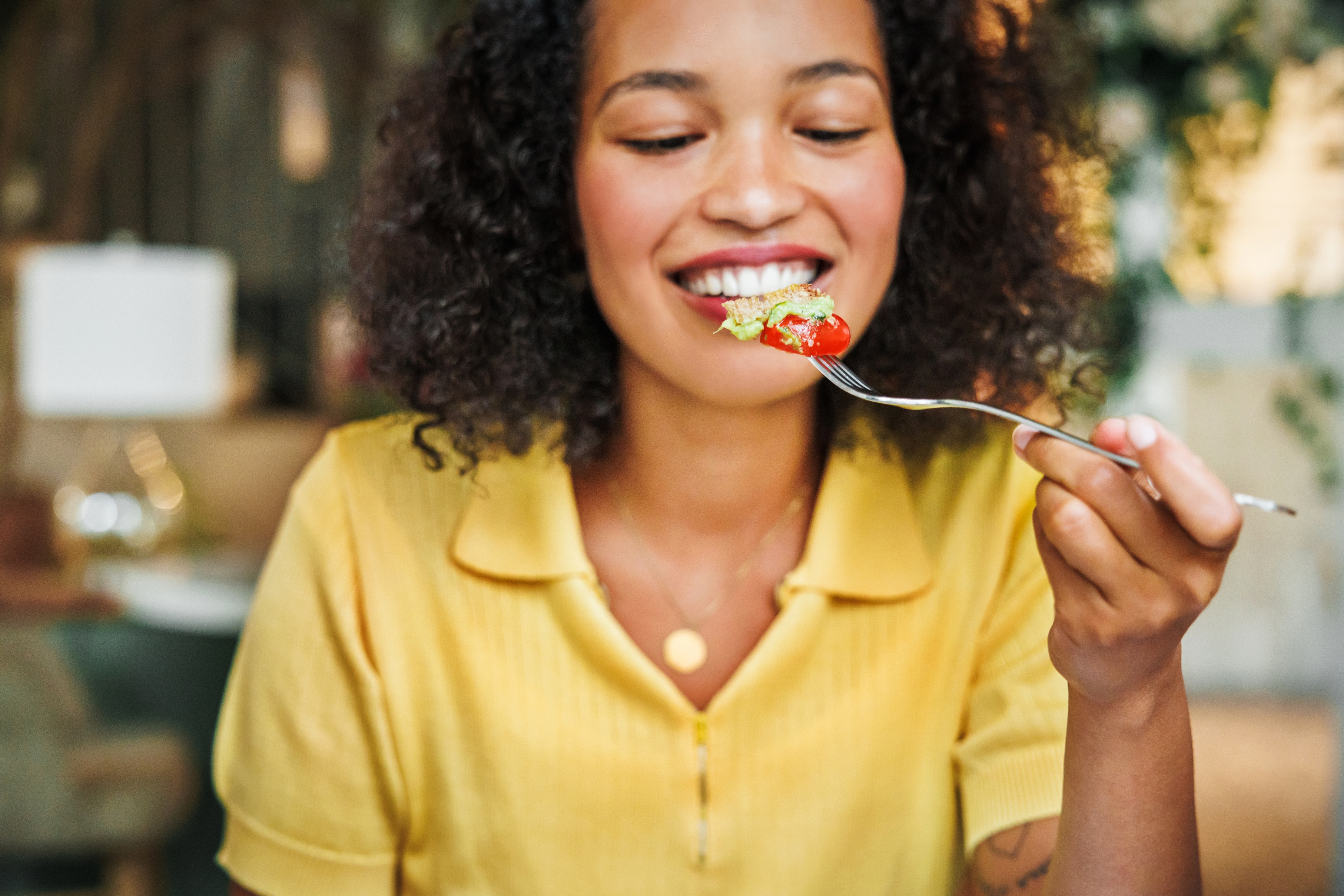Person smiling while holding a fork with salad, wearing a casual collared shirt