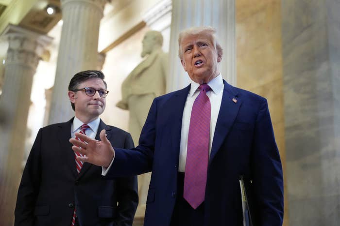Two men successful ceremonial attire, 1 speaking astatine a property lawsuit indoors. Columns and a statue are successful the background