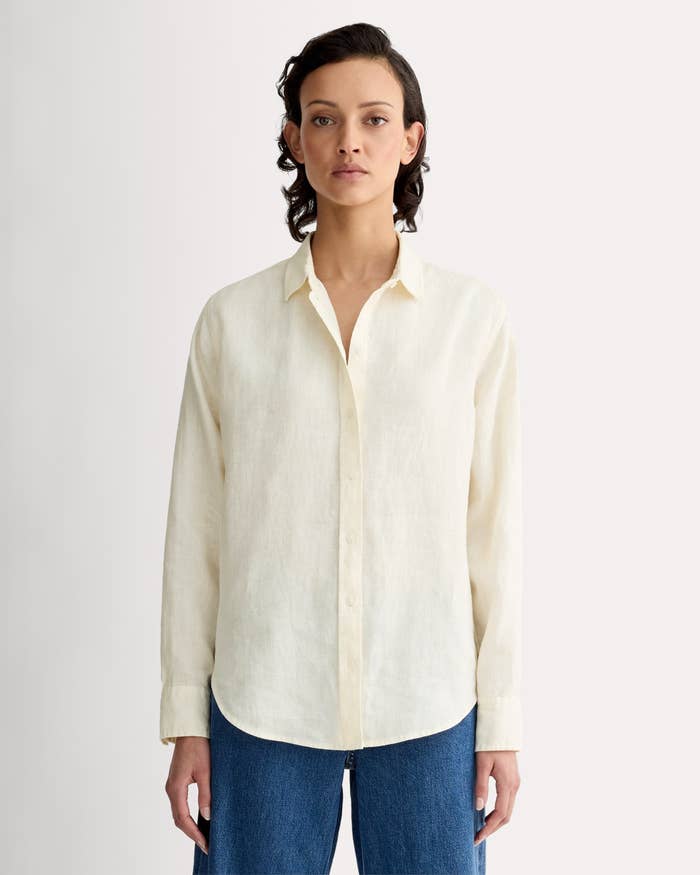 Person wearing a classical button-up garment with rolled sleeves and relaxed acceptable jeans, lasting against a plain background