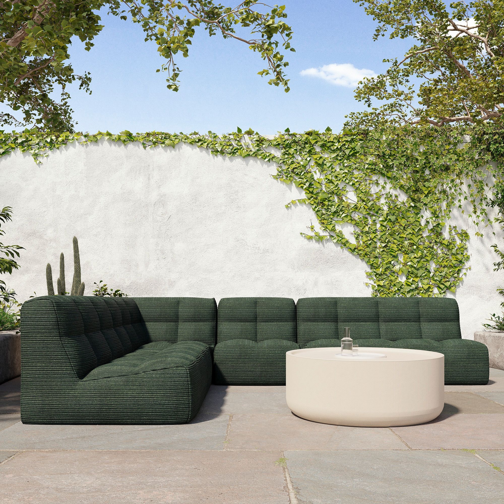 Outdoor patio with a modular, textured sectional sofa and a round coffee table, set against a white wall with lush greenery