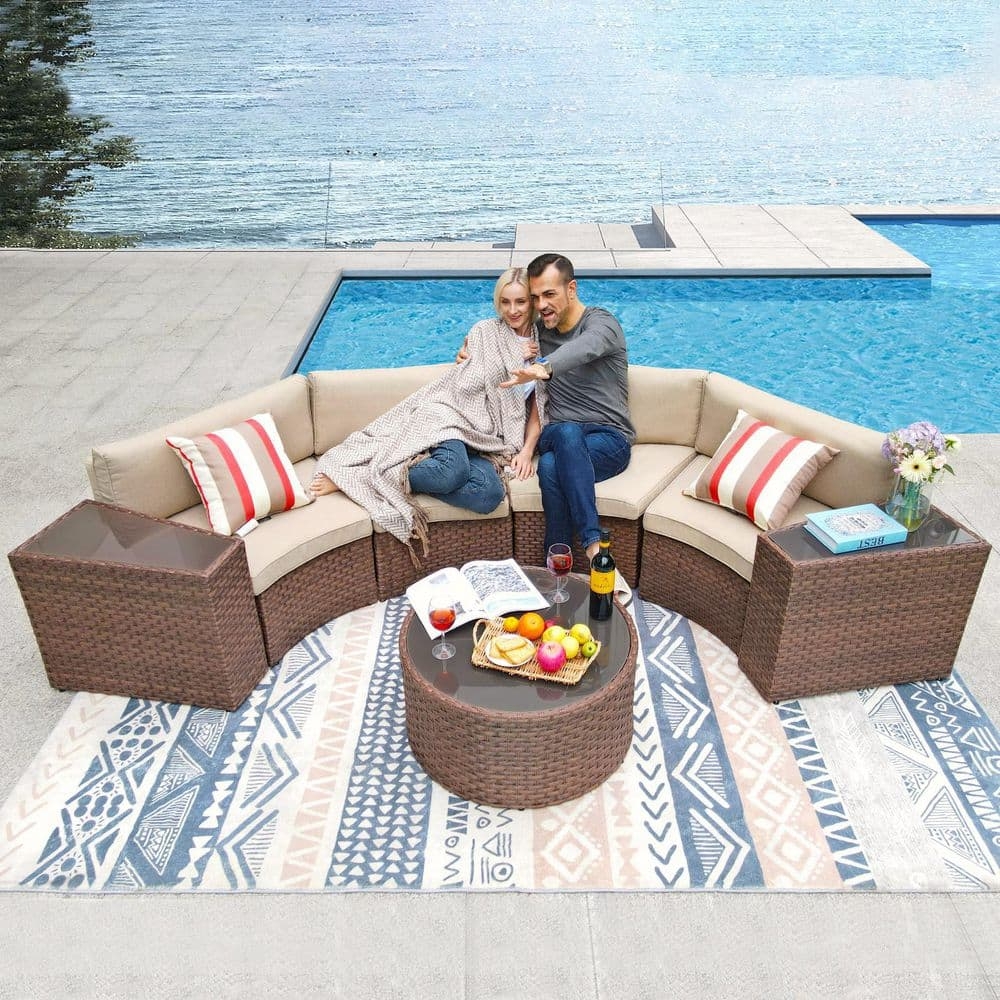 Couple sitting on a stylish outdoor wicker sectional by a pool, with a patterned rug, side tables, and a round coffee table holding fruit and drinks