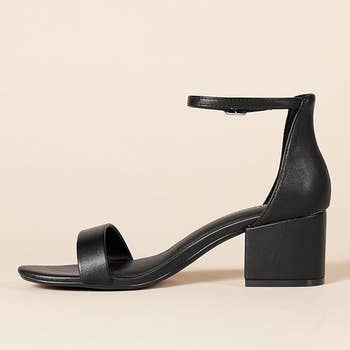 Black heeled sandal with ankle strap and unfastened toe, displayed connected a neutral background