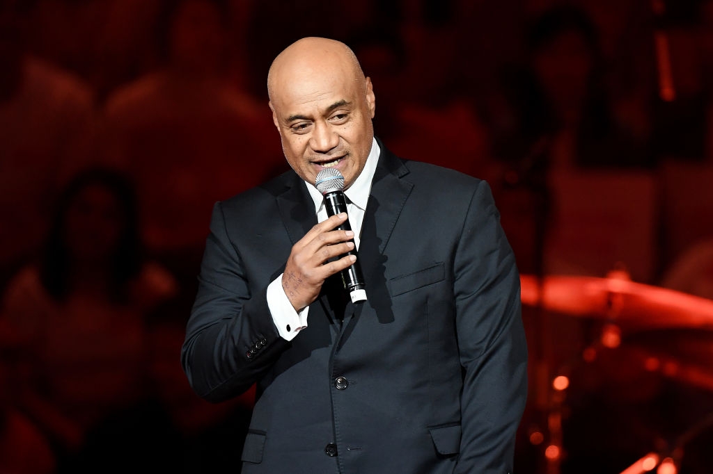 Person in a formal suit holding a microphone, speaking on stage at an event