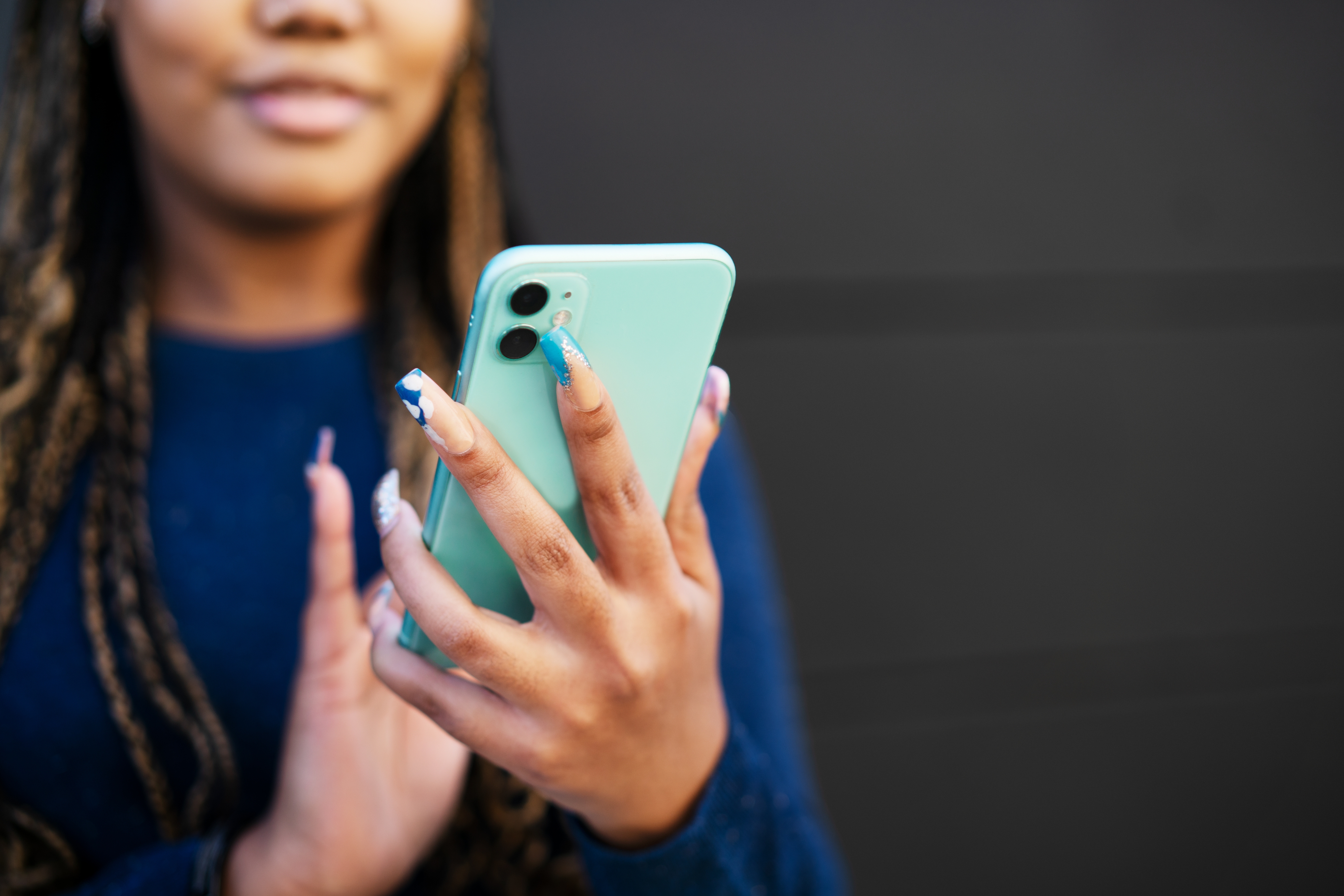 Person holding a smartphone, focusing on the screen with a neutral background. Their nails are manicured and styled