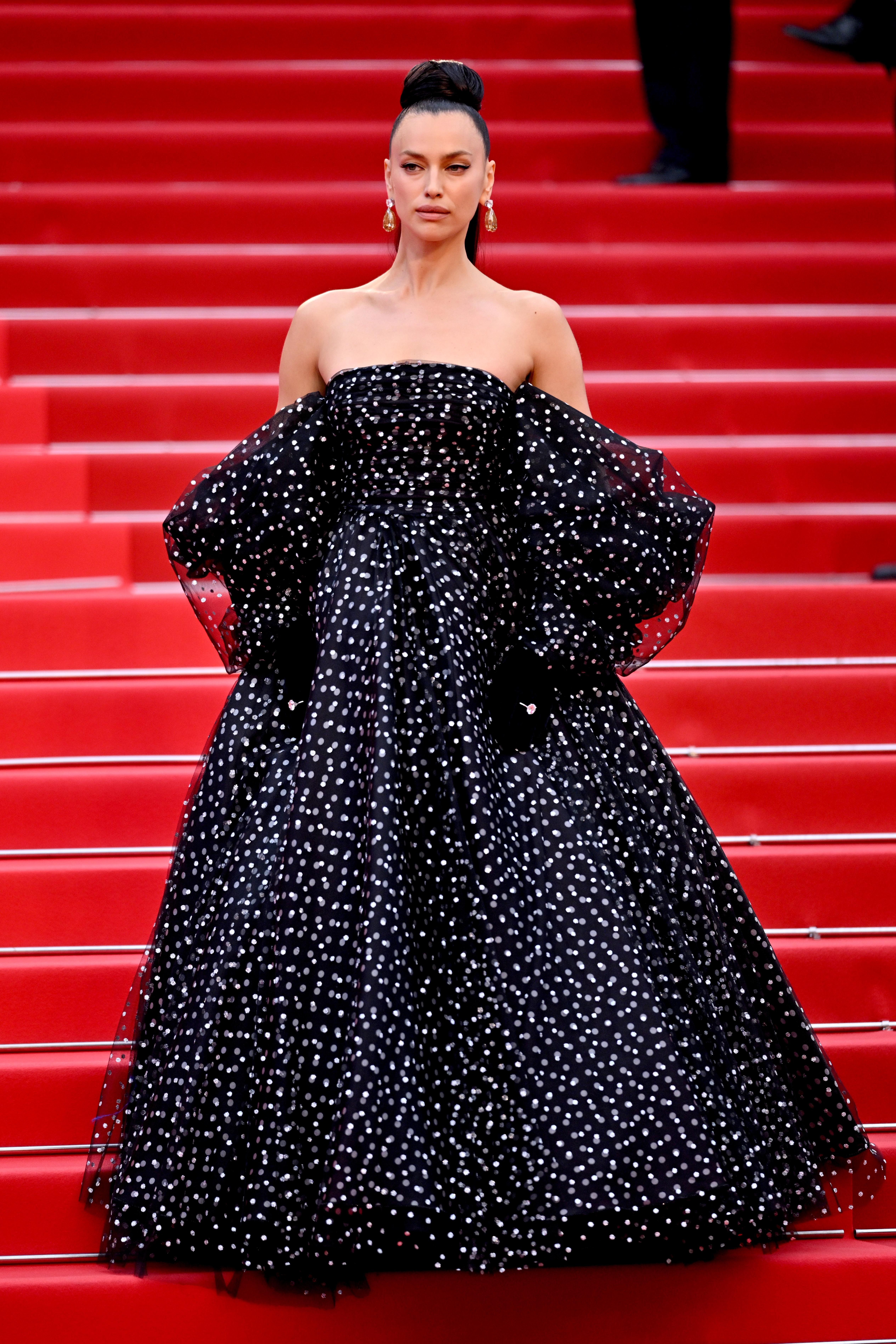 Irina Shayk on the red carpet wearing strapless, full-length gown with glittering polka dots and voluminous sleeves, with her hair in an elegant updo