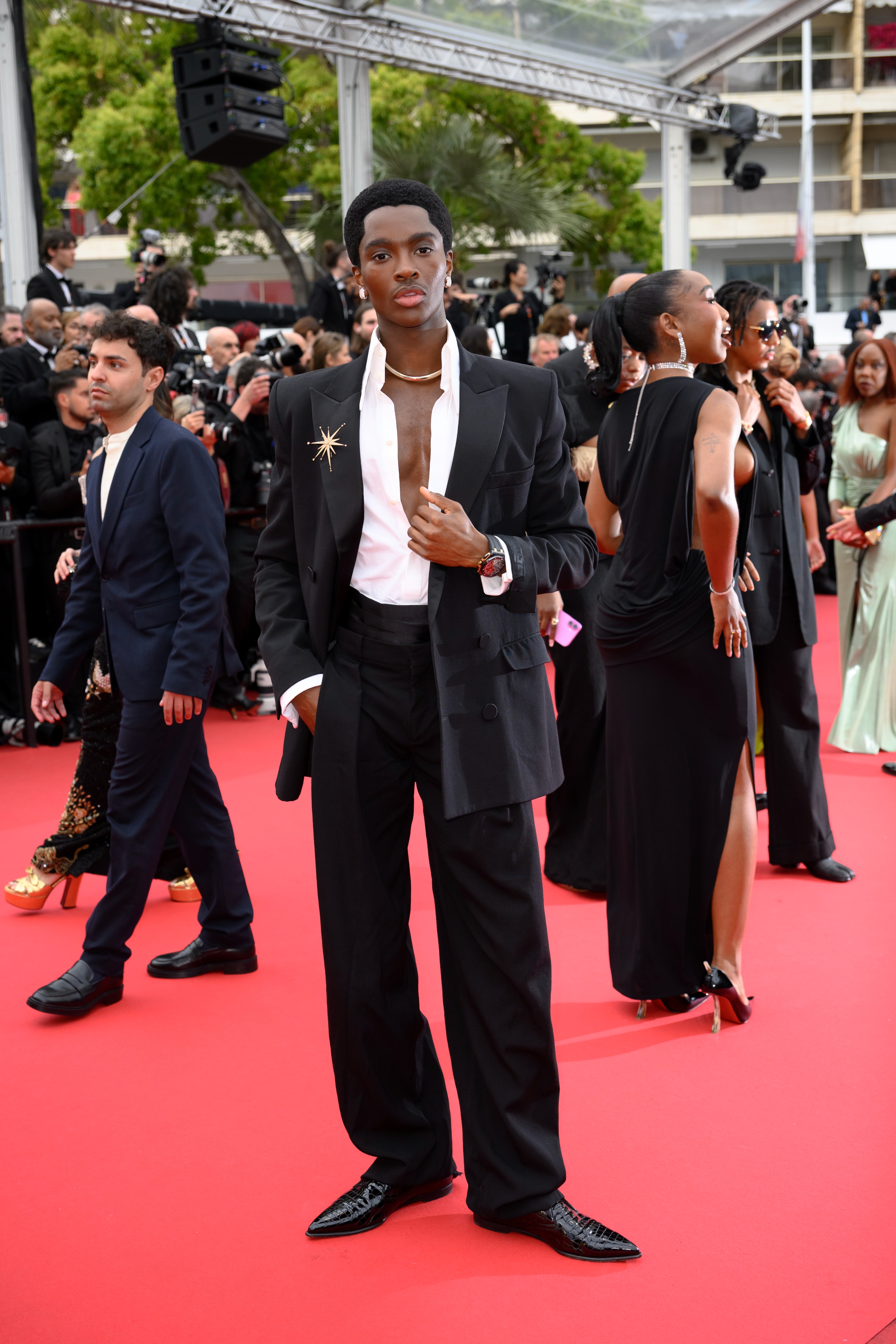 Alton Mason in a stylish suit with a star detail on the jacket, posing on a red carpet event, surrounded by others in elegant attire