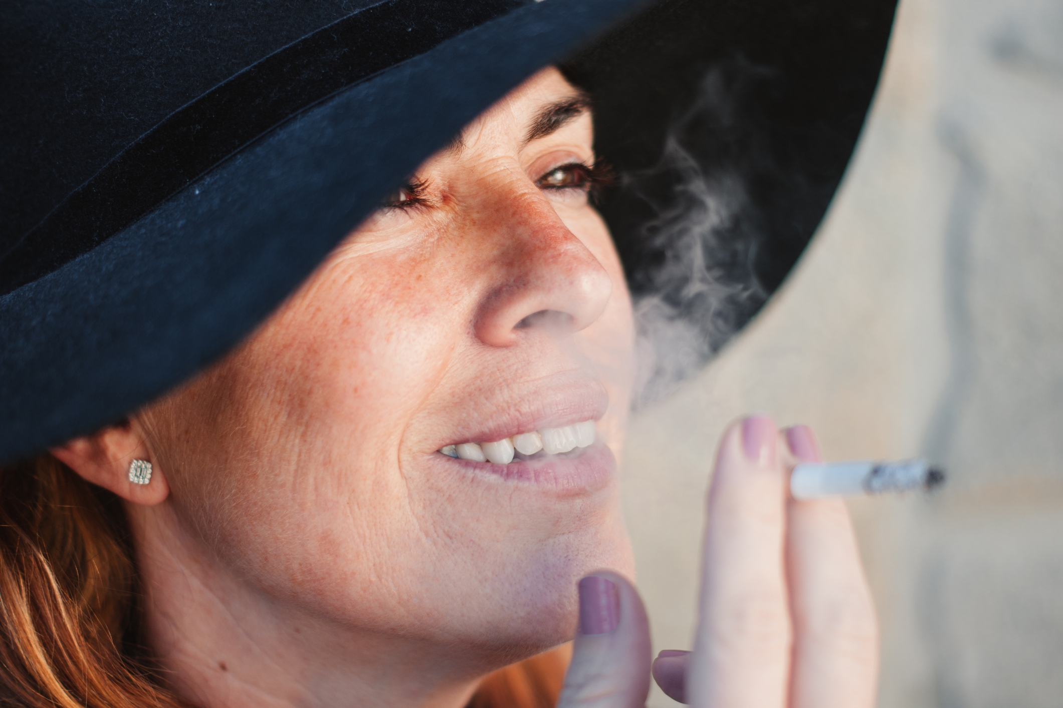 Personen som har en bred brennende hatt, smiler og holder en sigarett, med røyk synlig i nærheten av ansiktet