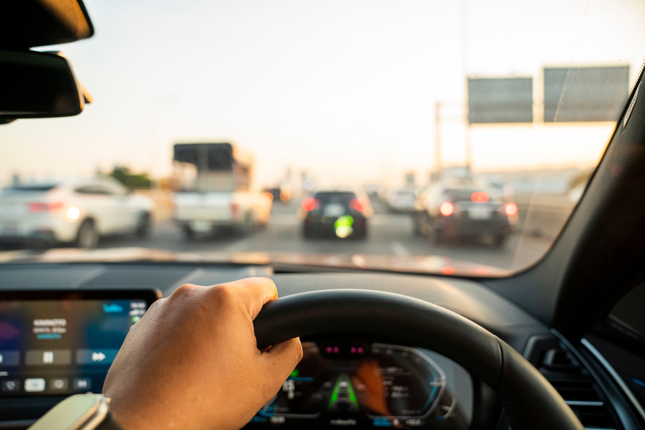 Driver's view from inside a car, hand on wheel, moving in heavy traffic on a busy highway with various vehicles ahead