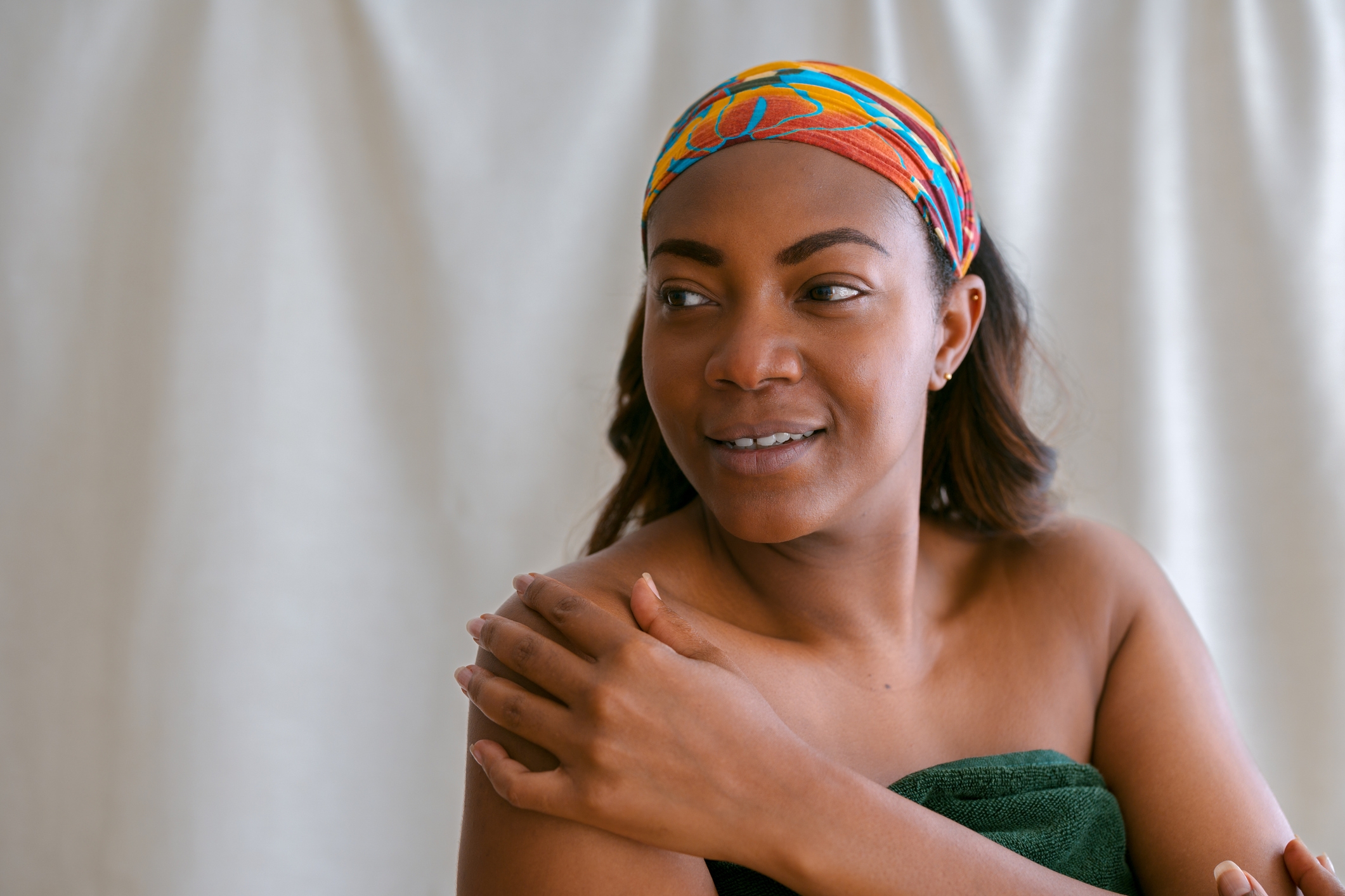 Person pakket inn i et håndkle, smilende forsiktig, med et fargerikt pannebånd. De ser ut til å være i en avslappet, egenomsorgsmessige omgivelser