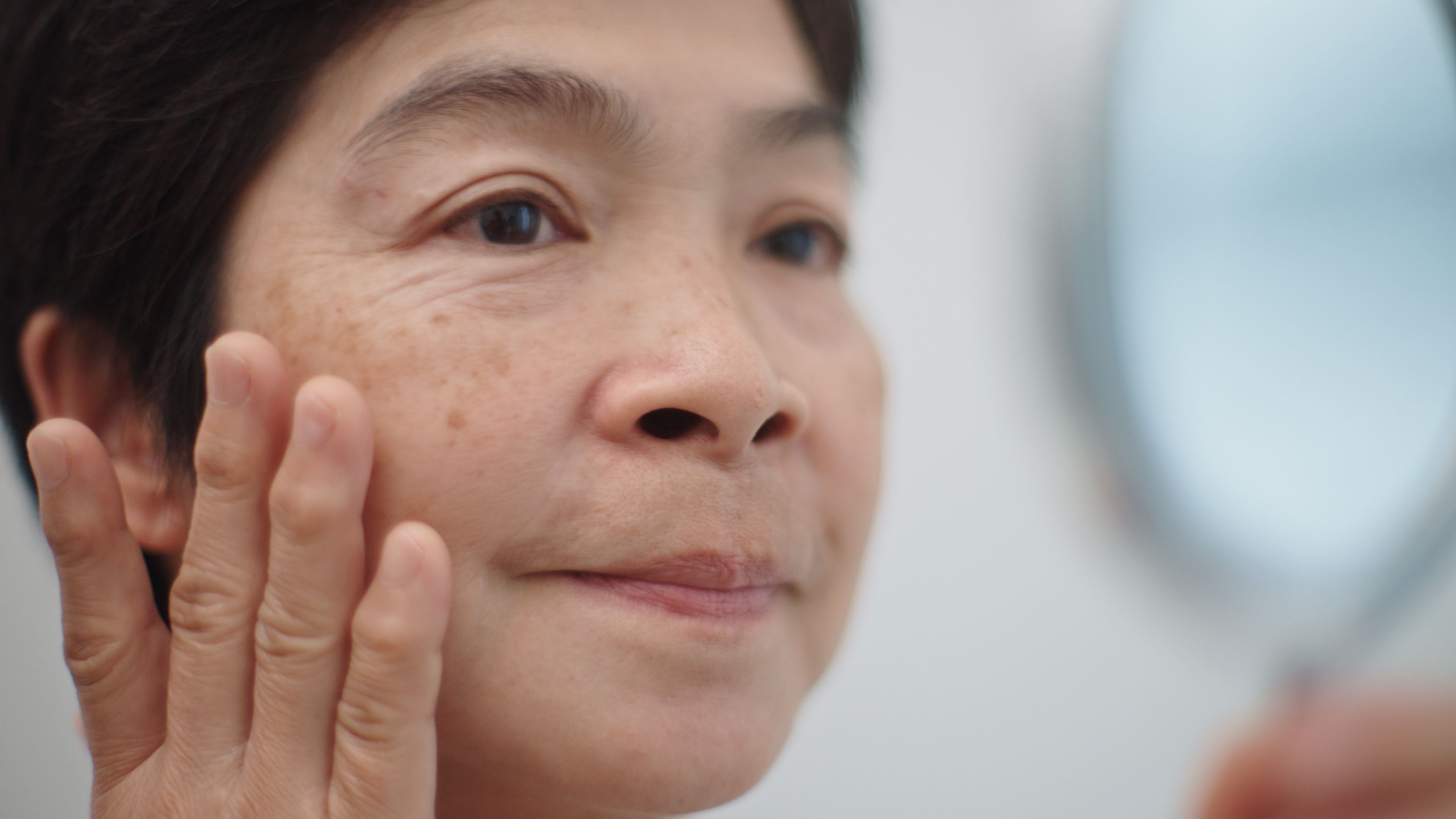 En person berører kinnet forsiktig mens han ser inn i et speil, og virker gjennomtenkt og introspektiv