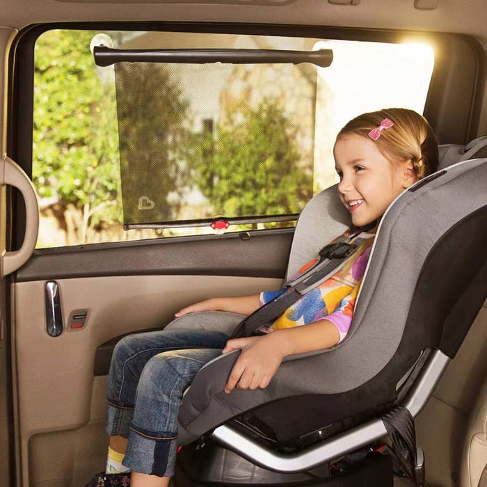 Child safely secured in a car seat inside a vehicle, smiling and looking out the window