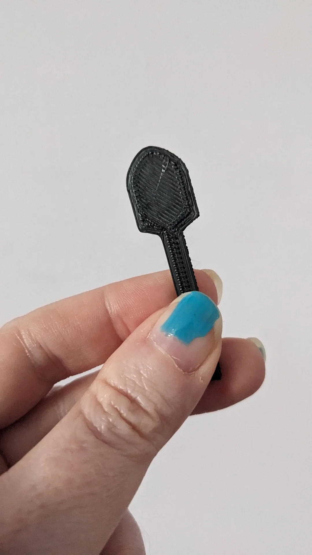 A hand holds a small black plastic spatula made for scooping skincare products out of the tube